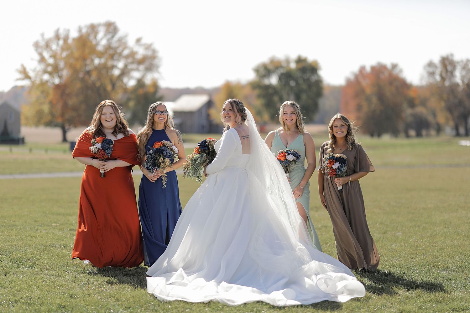 Wedding party gathered on grassy field during autumn outdoor celebration.