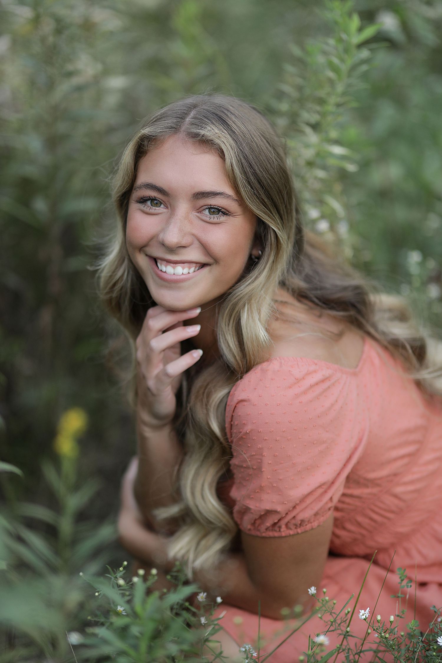 A person in a peach-colored dress poses outdoors among greenery in a series of candid portrait shots.