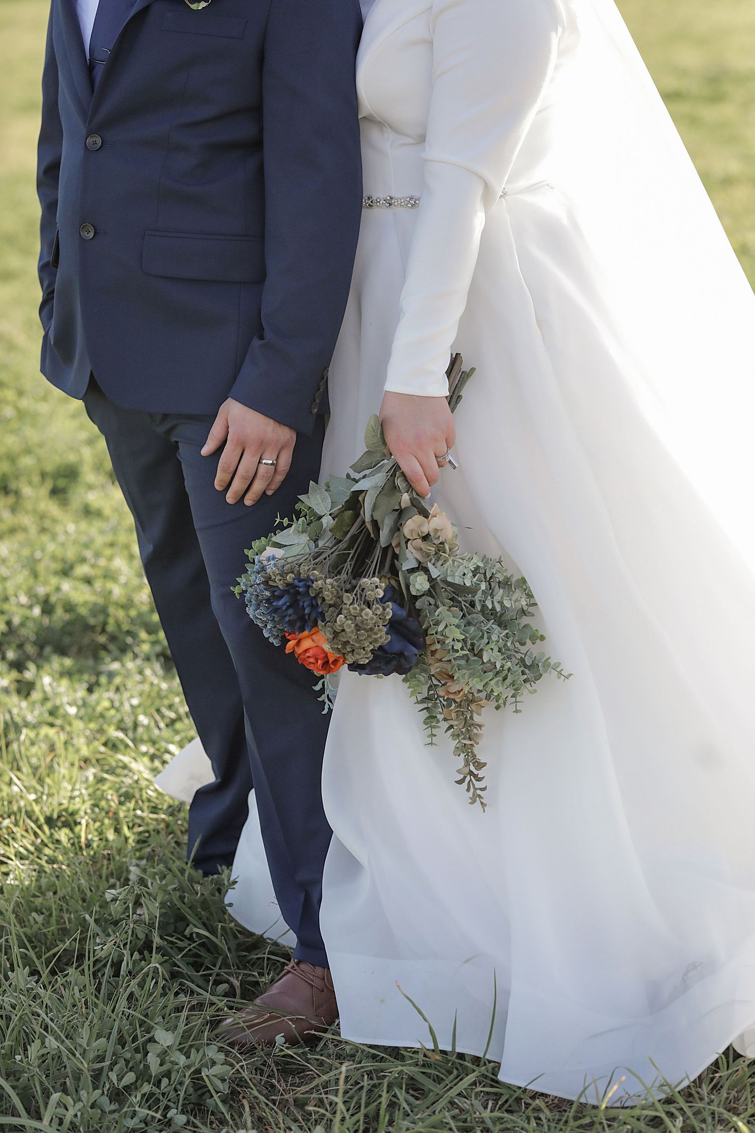Detail shot of wedding couple showing navy suit and white dress with blue and orange floral bouquet.