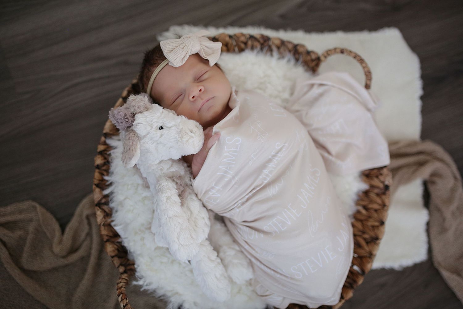 A sleeping baby swaddled in white fabric lies peacefully in a woven basket with soft bedding.