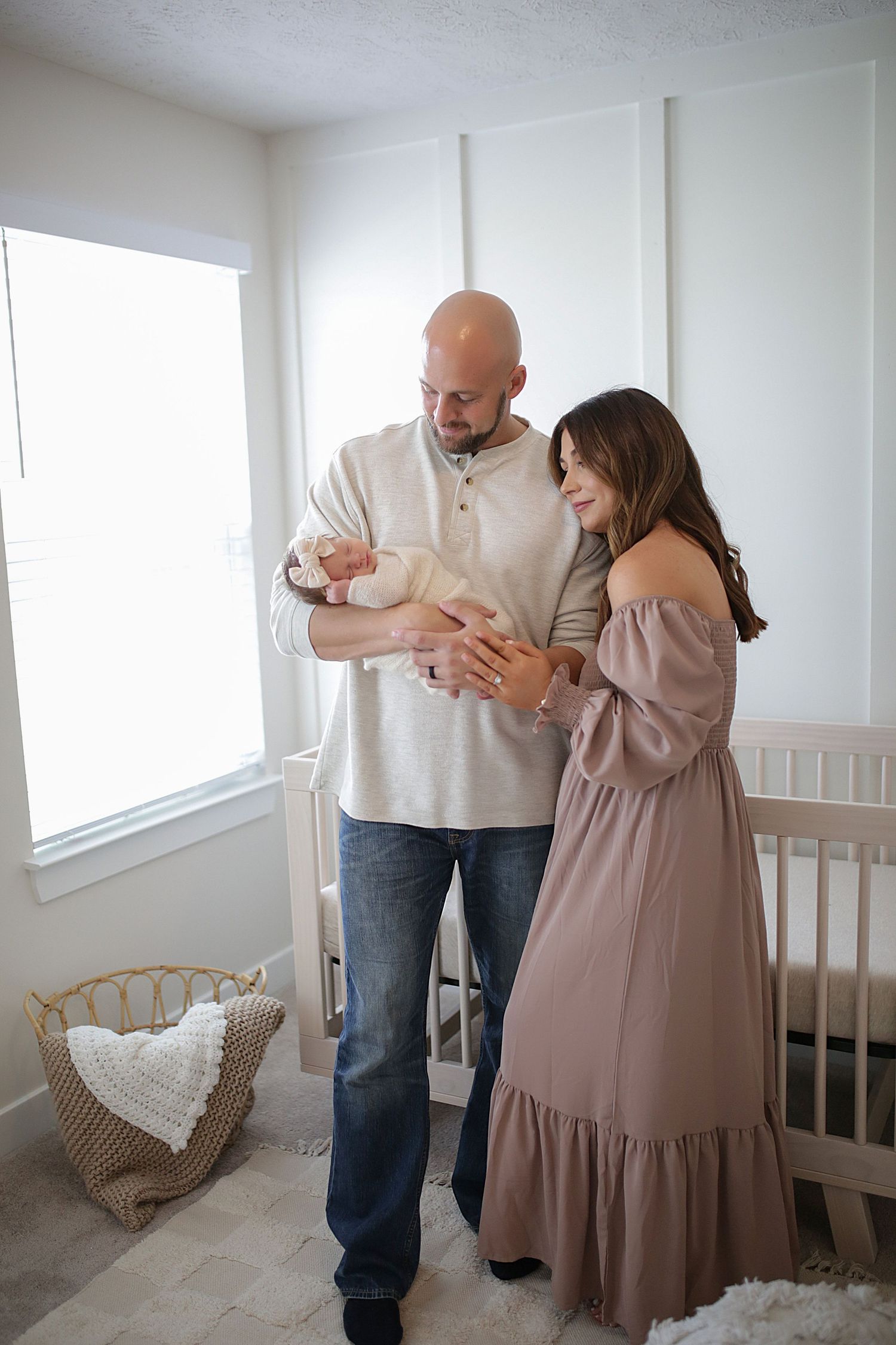 A couple sharing an intimate moment in a nursery room with white walls and a wooden bassinet.