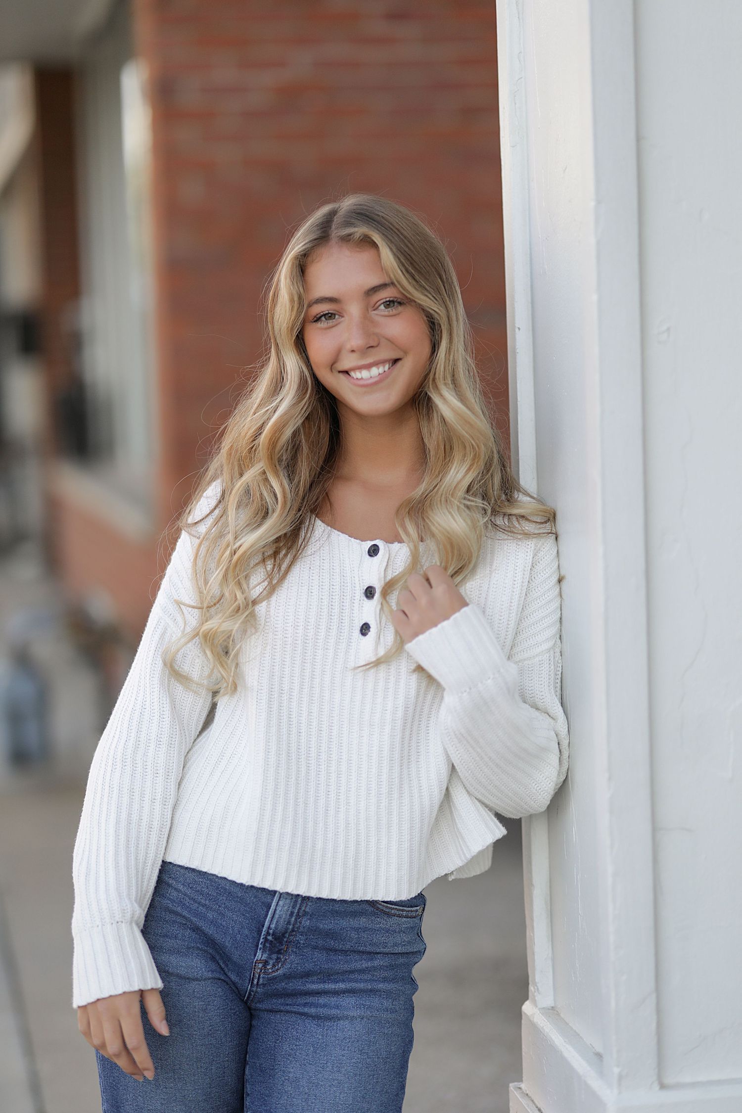 Person in white sweater and jeans posing casually against white pillars.