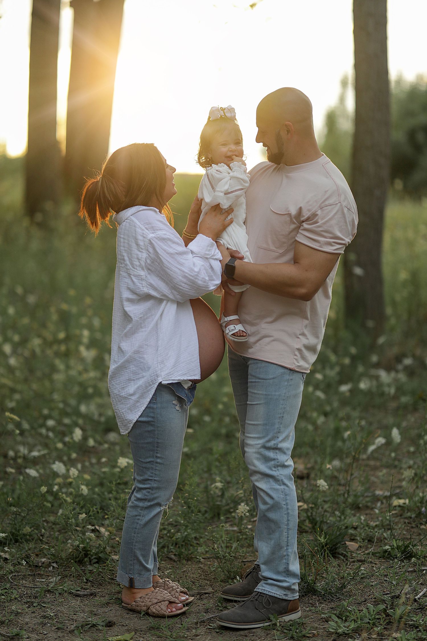 Two people dance and embrace tenderly in a sunlit field with wildflowers during golden hour.