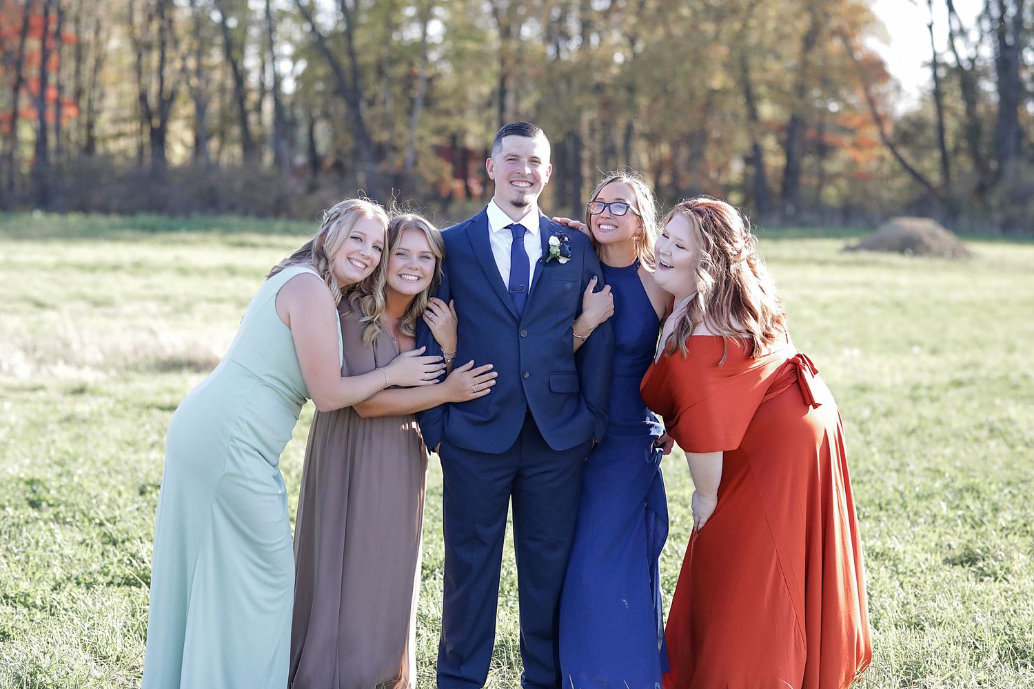 Group photo session in a fall field with wedding party wearing coordinating formal attire.