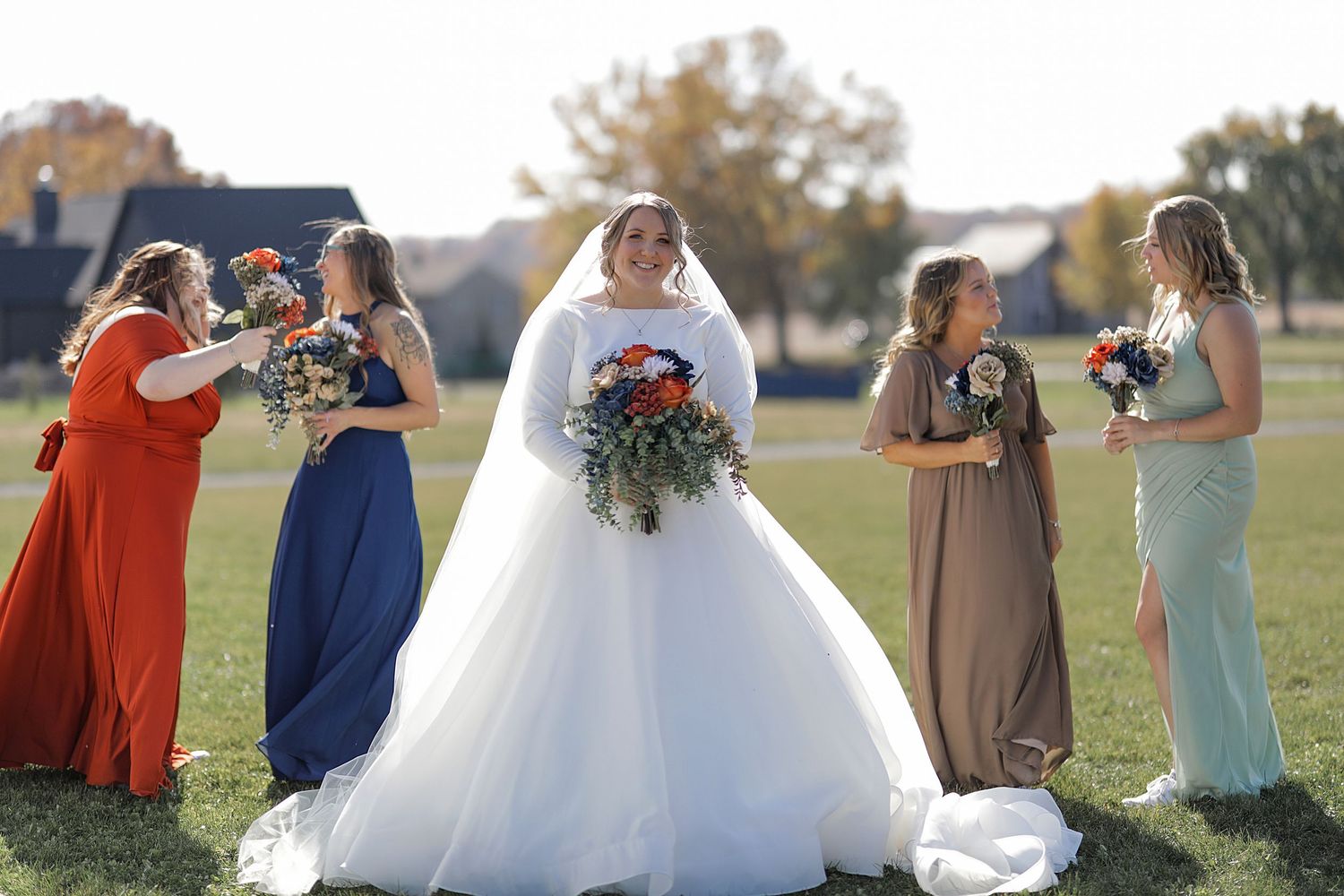 Bridal party in colorful dresses poses together on sunny autumn day.