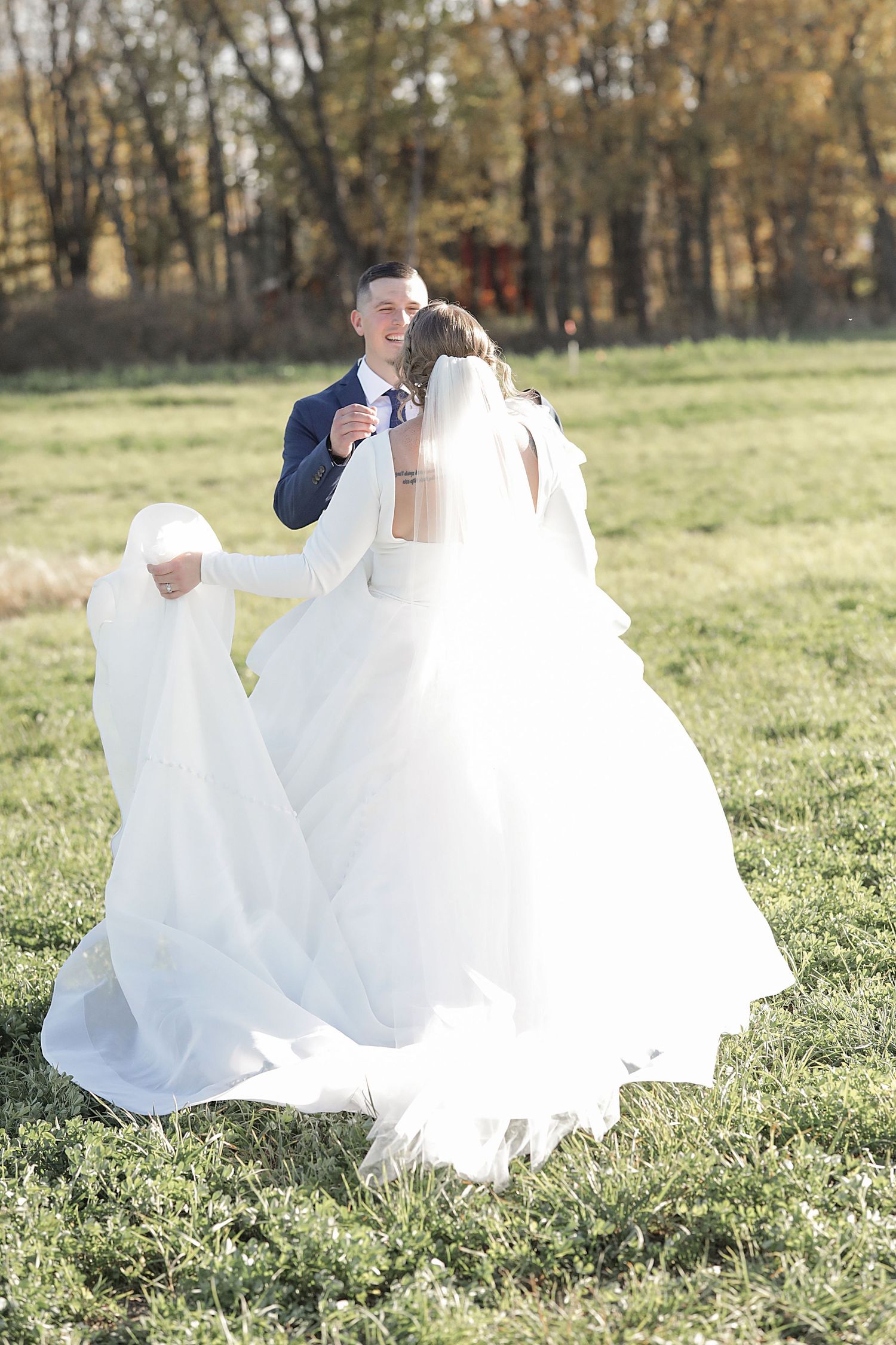 Bride's white dress flows elegantly across green grass during outdoor photo session.