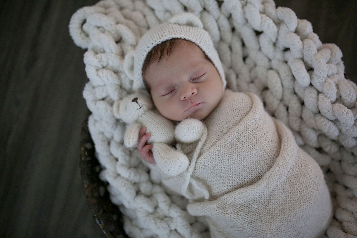 Peaceful sleeping newborn swaddled in cream-colored wrap on chunky knit blanket.