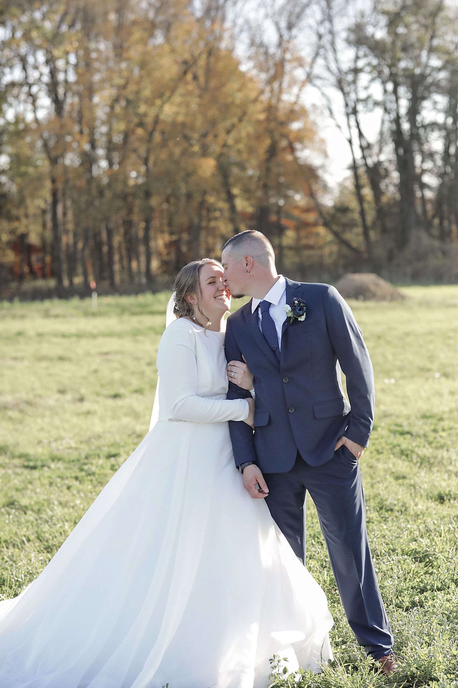 A romantic wedding photo of newlyweds embracing in an autumn field with golden trees.