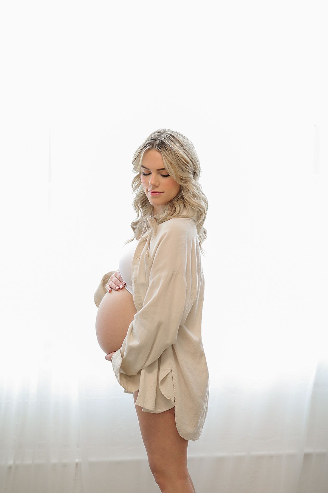 Light and airy maternity boudoir photos in cream colored button-down shirt against white background.