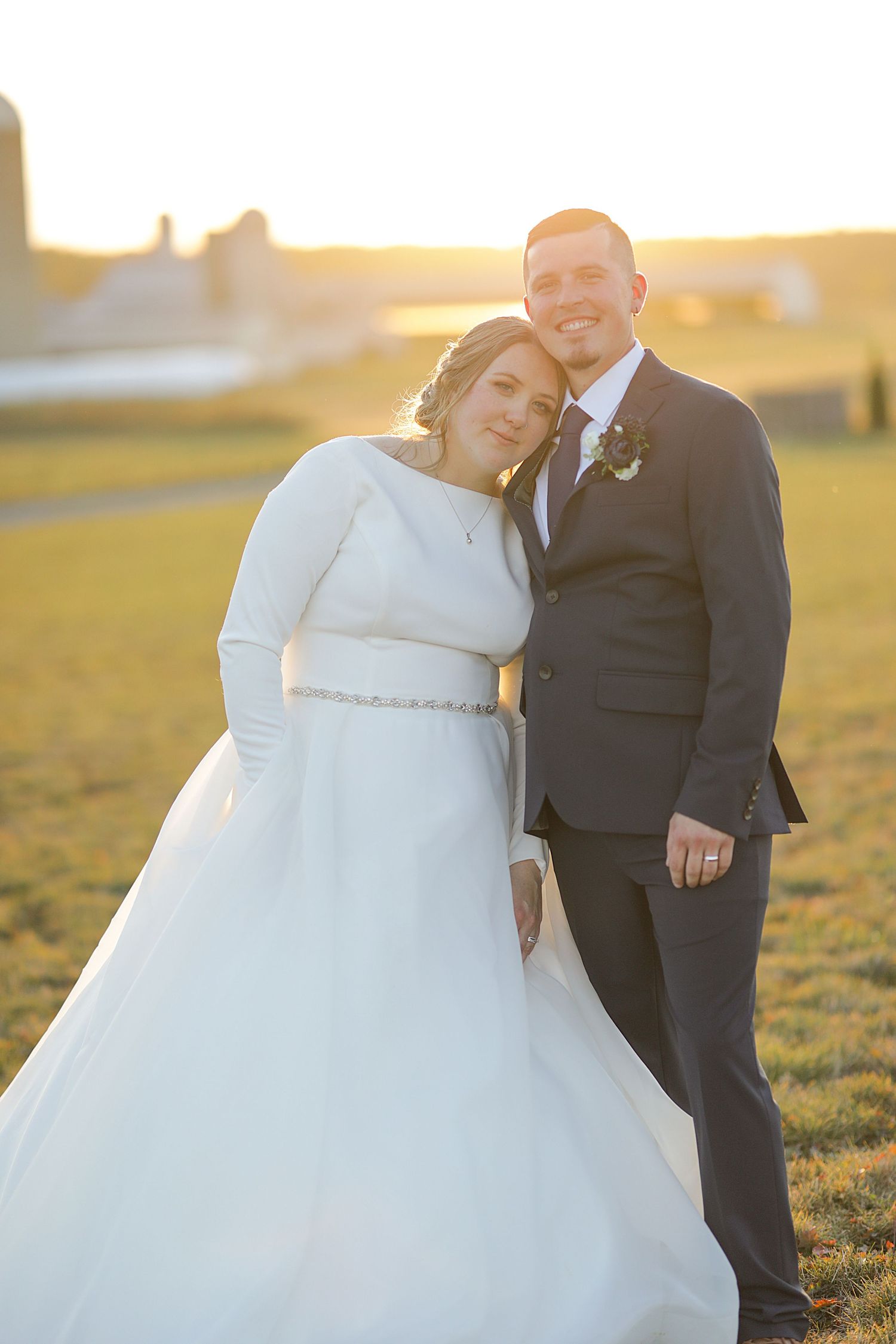 Newlyweds pose together in warm sunset light with bride wearing elegant long-sleeved wedding gown.