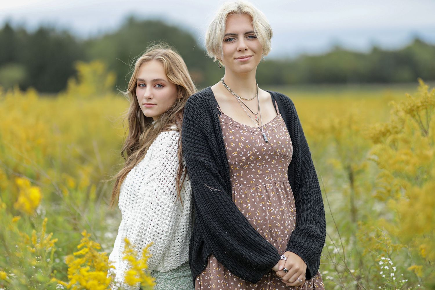A group of people stand together in a blooming yellow flower field on a sunny day while wearing casual clothing.