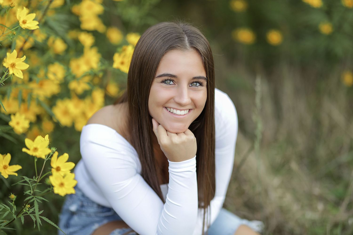 Yellow flowers bloom in foreground of outdoor photo session against natural backdrop.