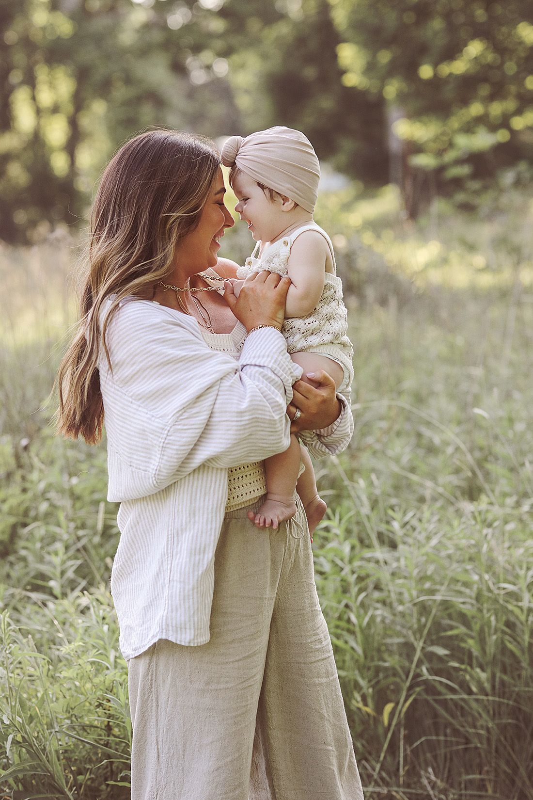 A tender moment between parent and baby in a sunlit meadow wearing light colored clothing.
