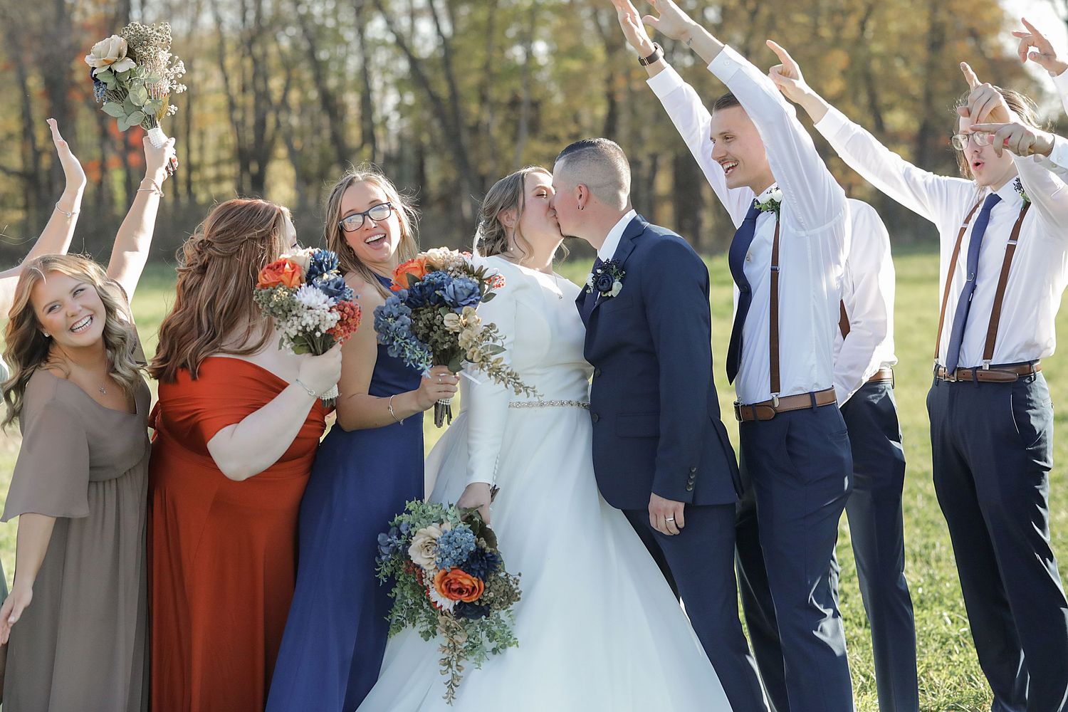 Celebratory wedding party moment under white pergola with colorful autumn backdrop.
