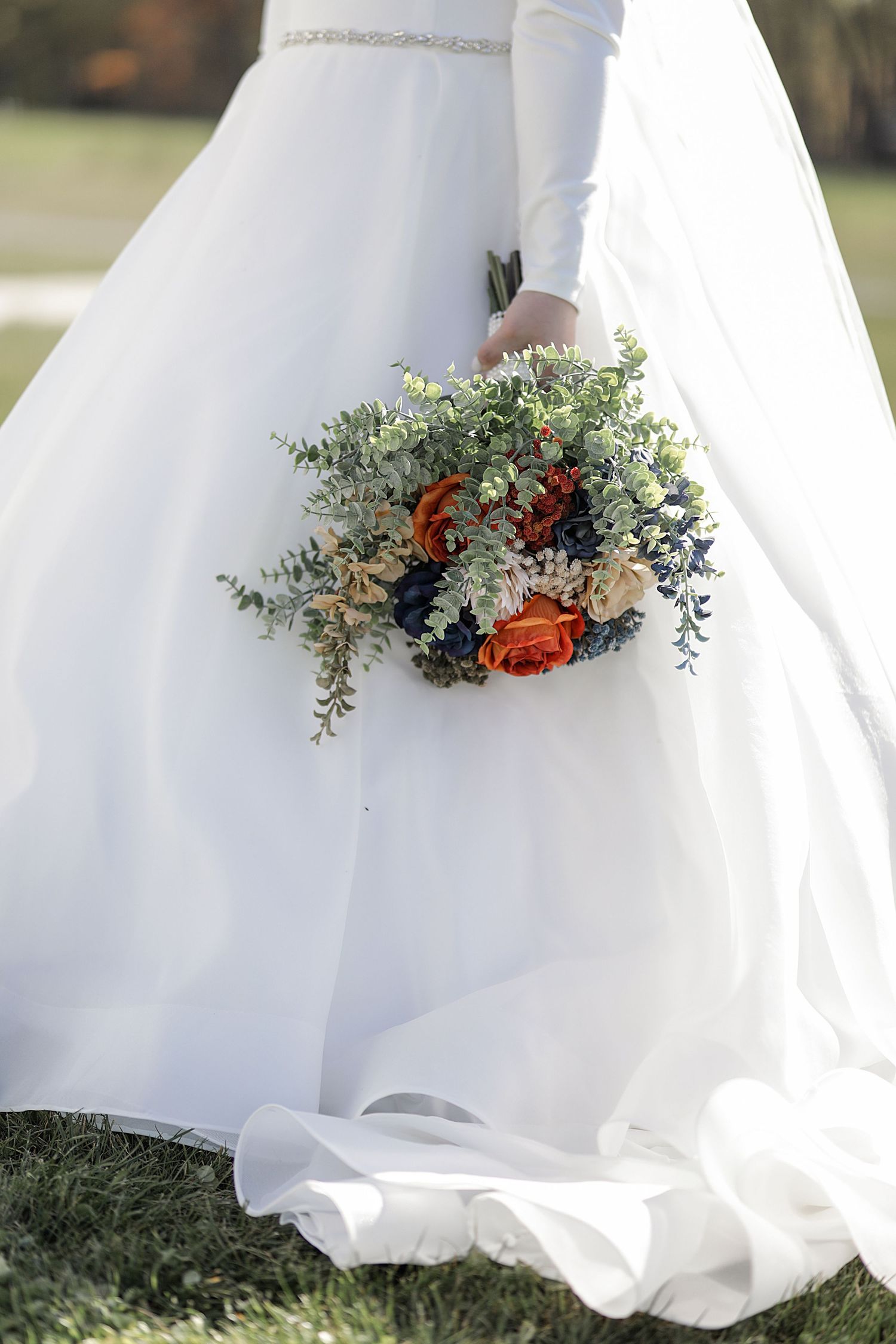 Bottom of white wedding dress decorated with greenery and orange floral accents.