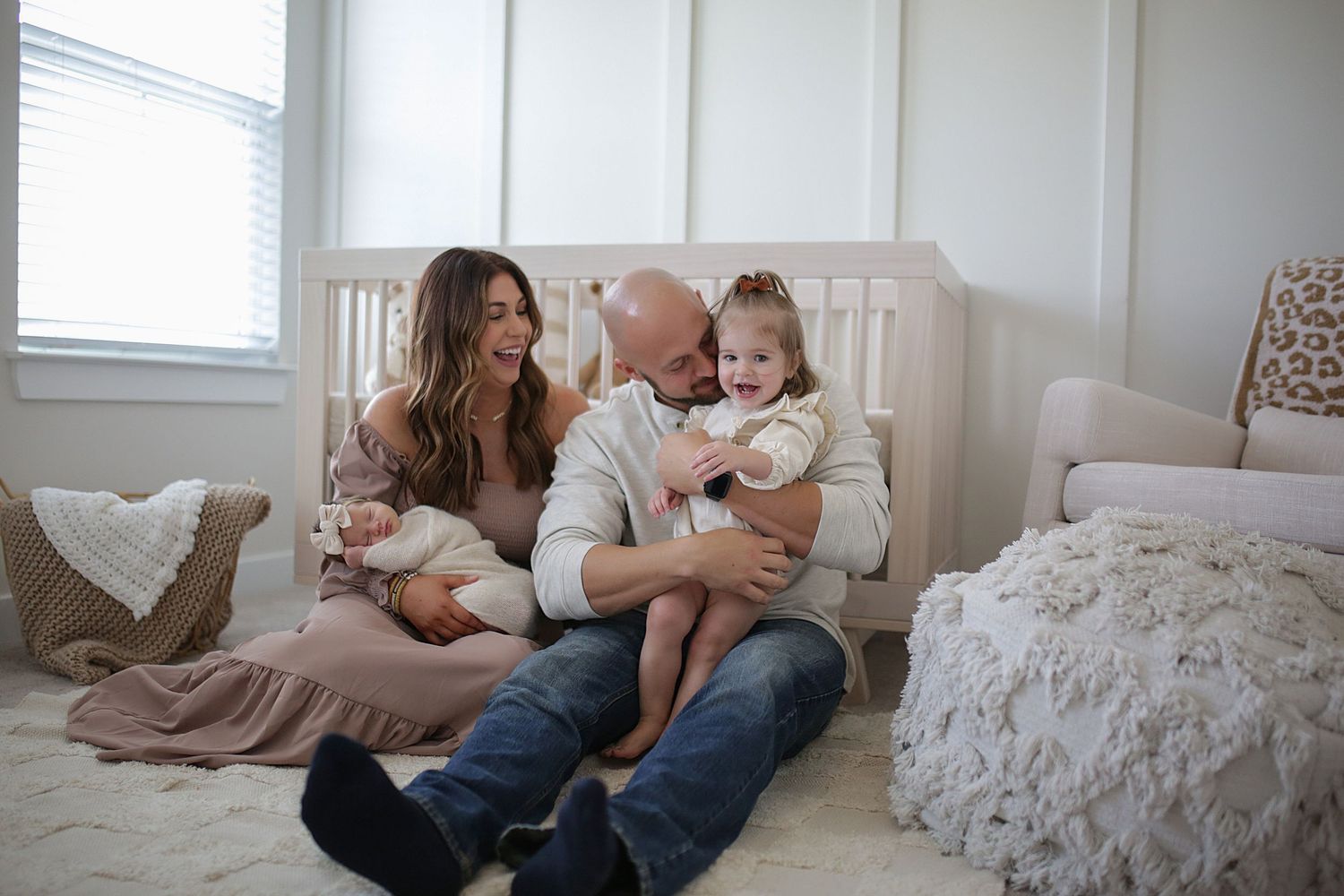 A family sits together on the floor of a bright bedroom sharing joyful laughter and cuddles.