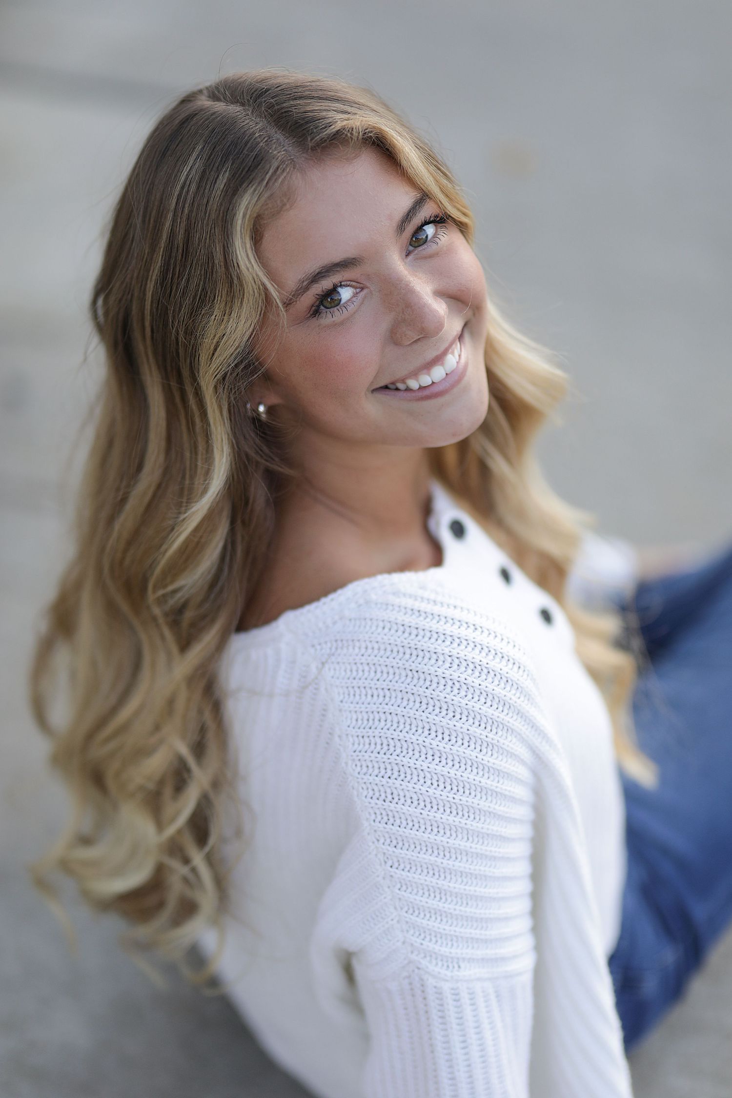 Someone wearing a white knit sweater poses against a light background with soft waves in their hair.