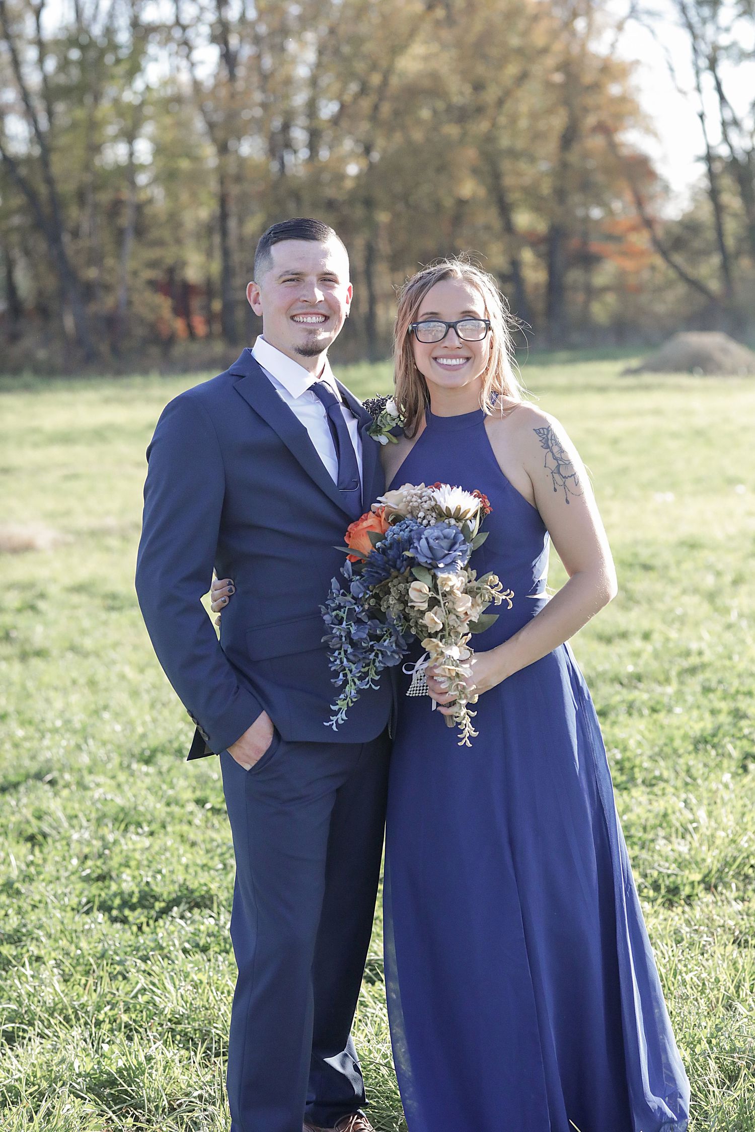 Wedding party in navy blue attire posing together in sunny outdoor field.
