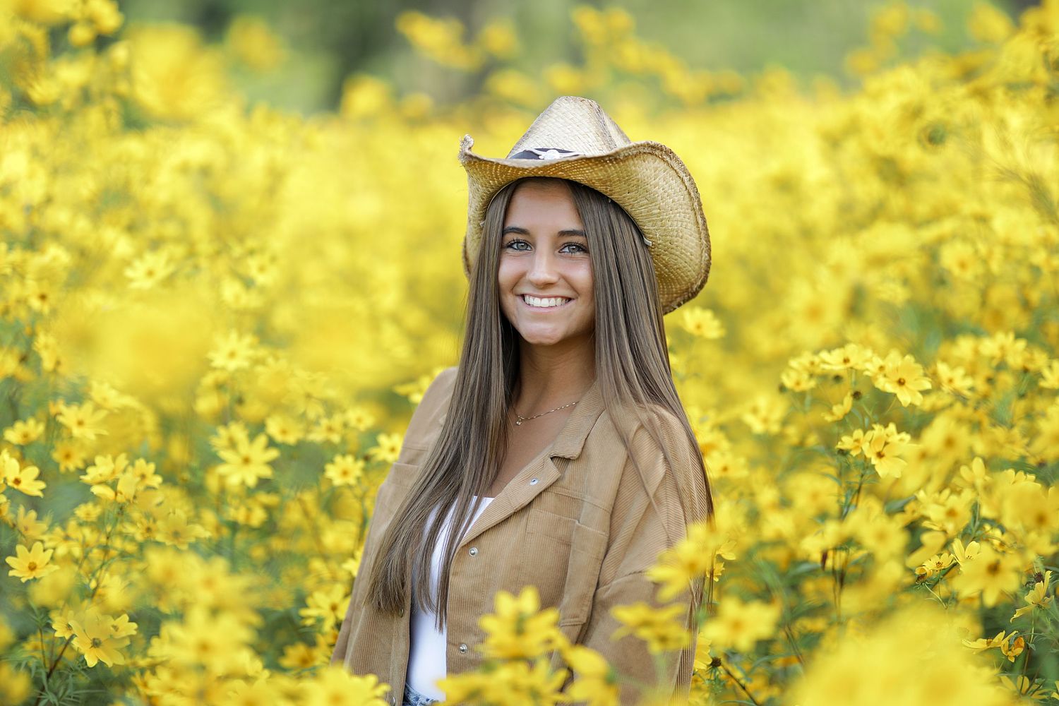 A person wearing a cowboy hat poses in a vibrant yellow canola field on a sunny day.