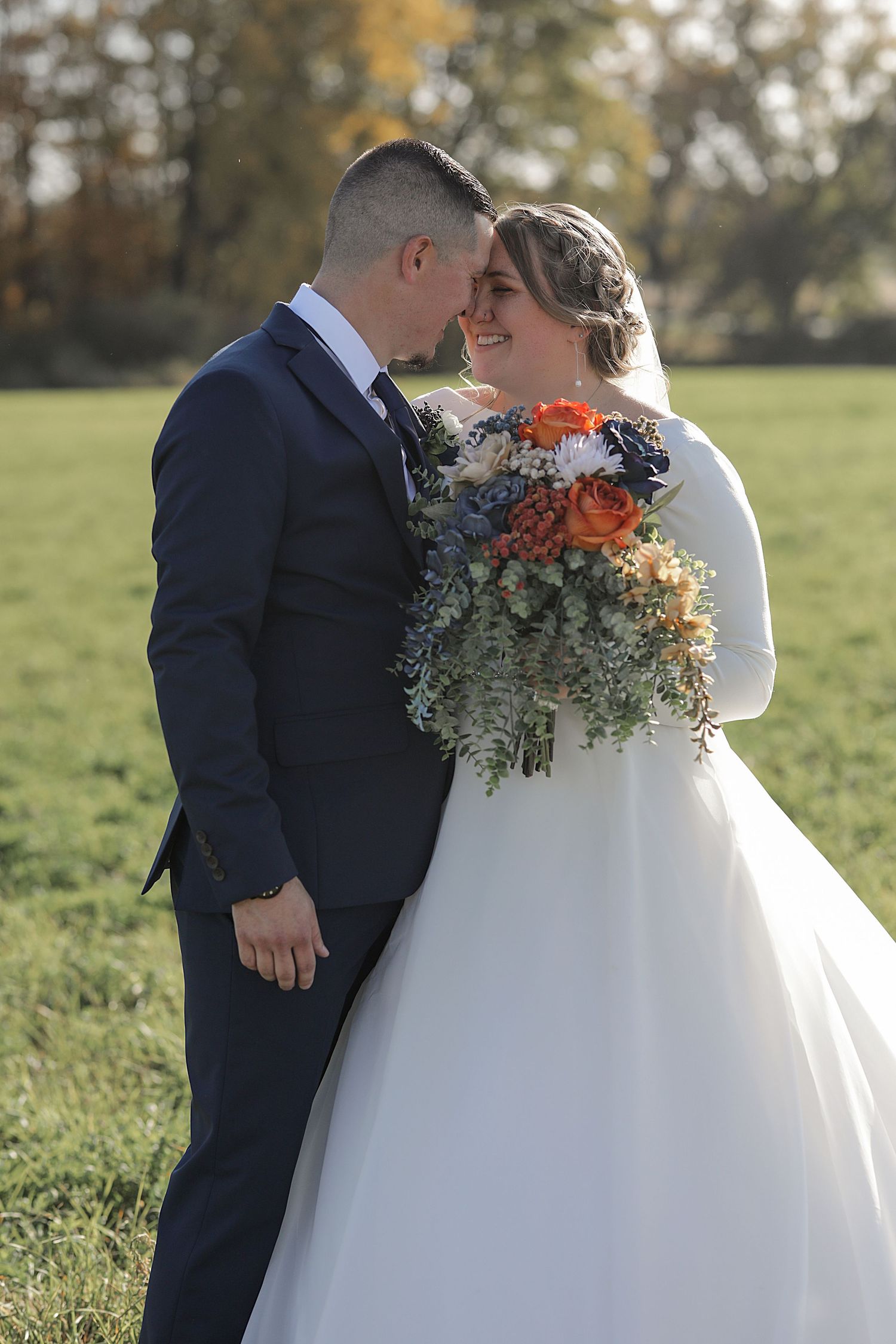 Newlyweds posing together in field with autumn-colored floral bouquet.