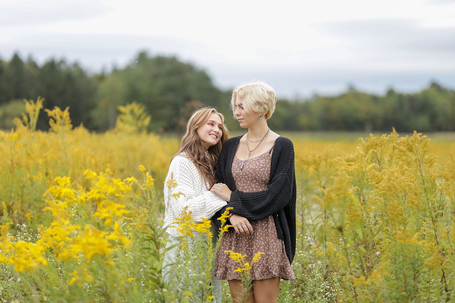 Two people standing together in a vibrant yellow wildflower field on an overcast day.