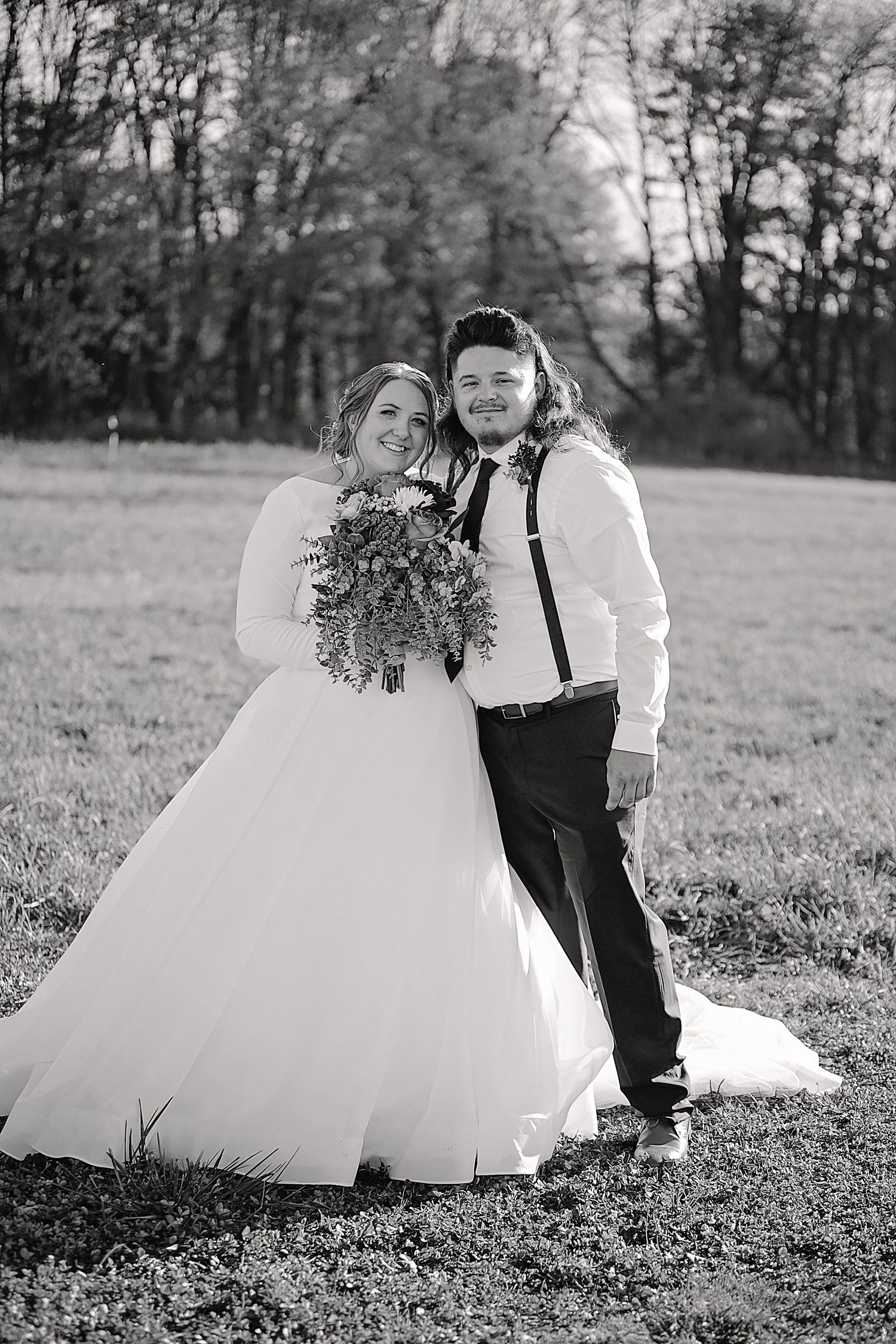 Black and white wedding portrait of couple with bride holding rustic bouquet in outdoor setting.