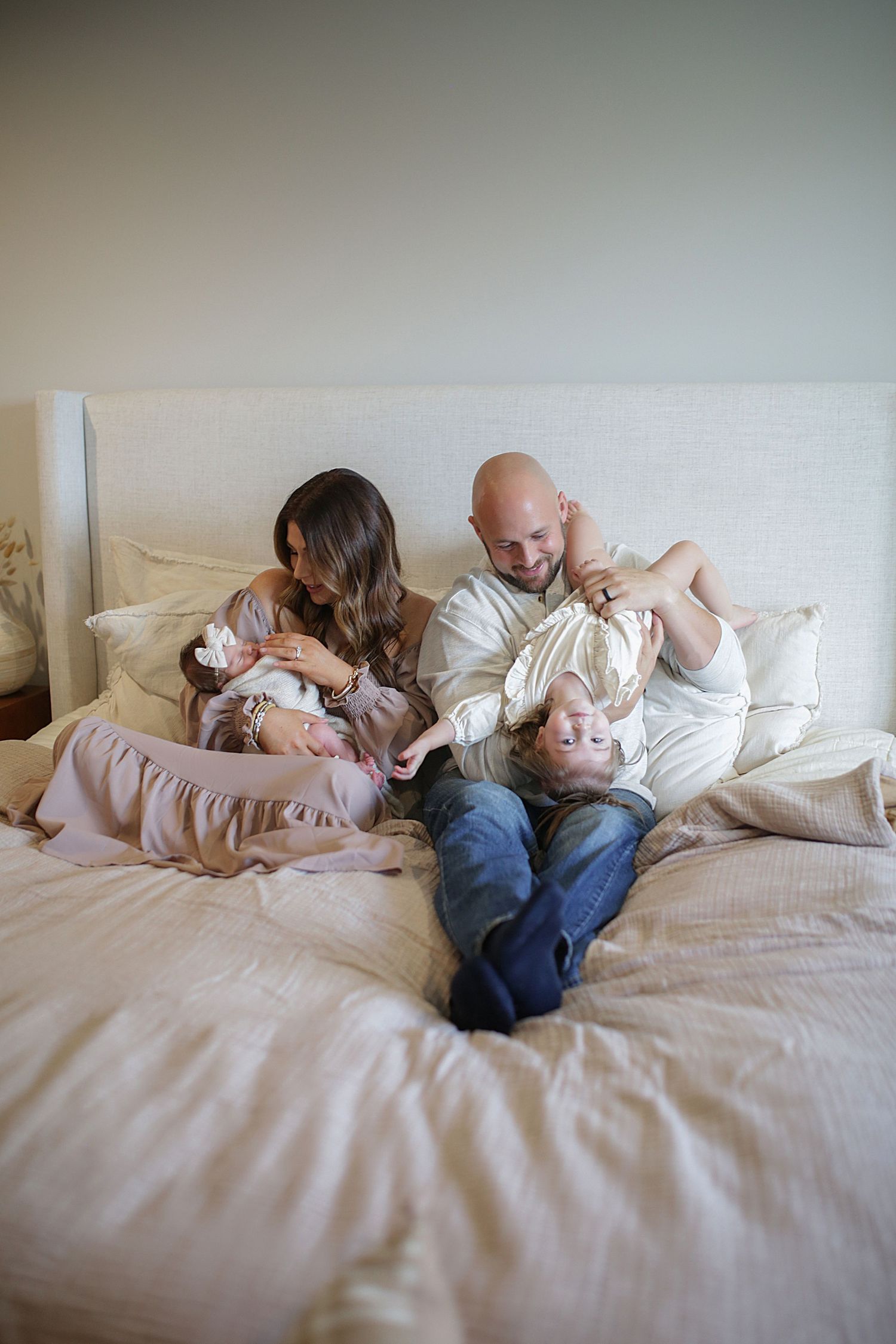 A family relaxes together on a cozy white bed with soft linens and pillows.