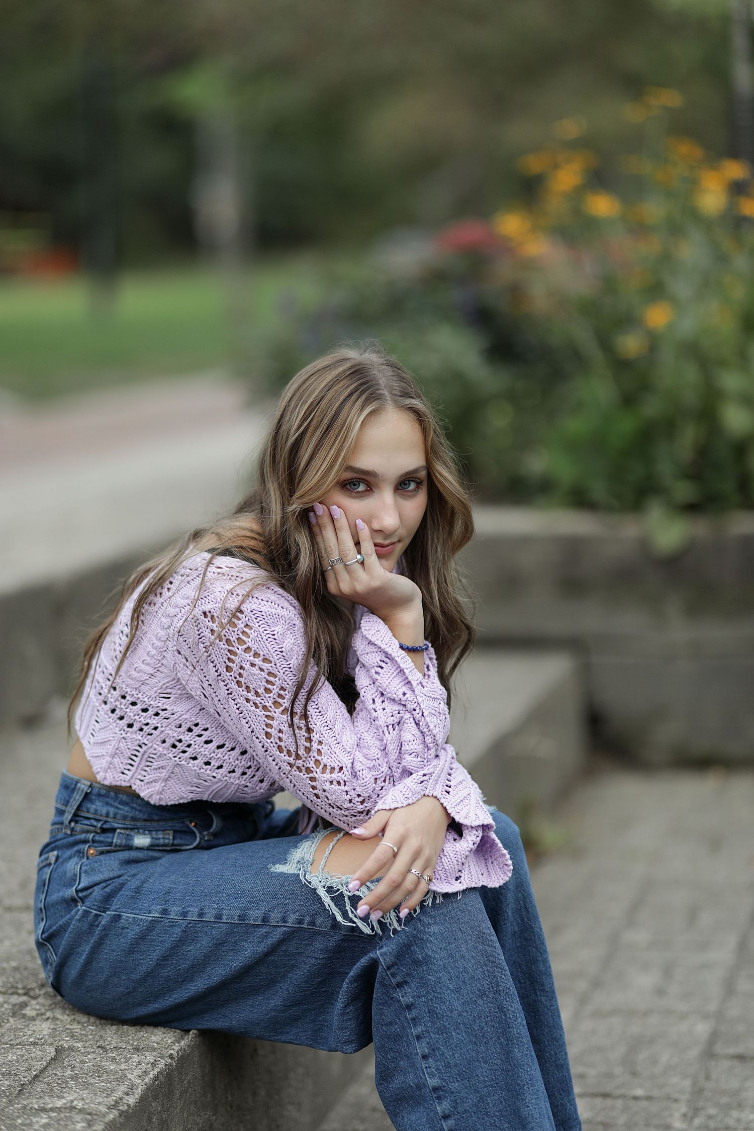 Someone wearing a pink knit sweater and jeans sits thoughtfully on concrete steps in an outdoor garden setting.