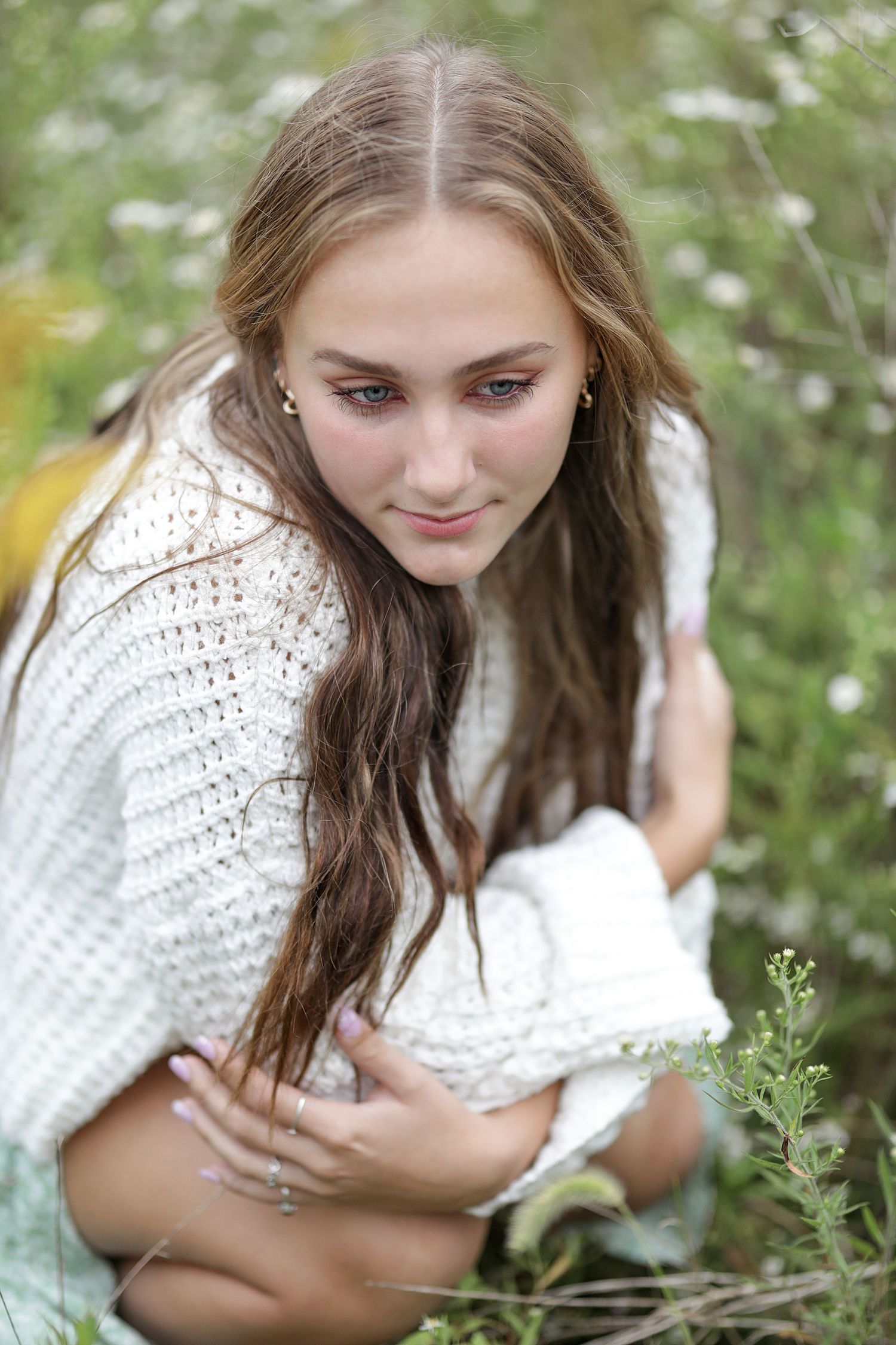 A soft portrait in a wildflower meadow with someone wearing a cozy white knit sweater among delicate blooms.