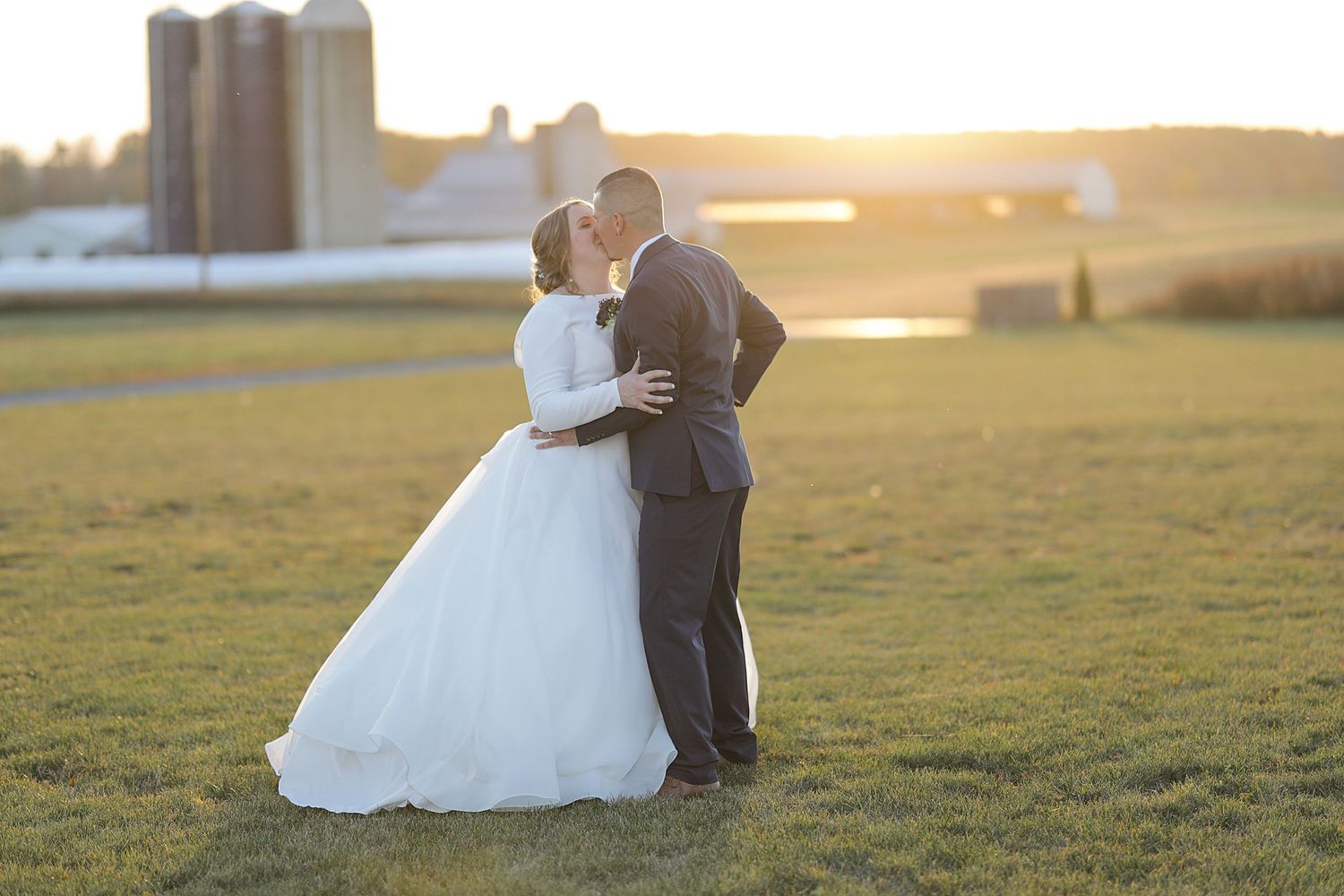 Newlyweds embracing in a sunlit field during golden hour.