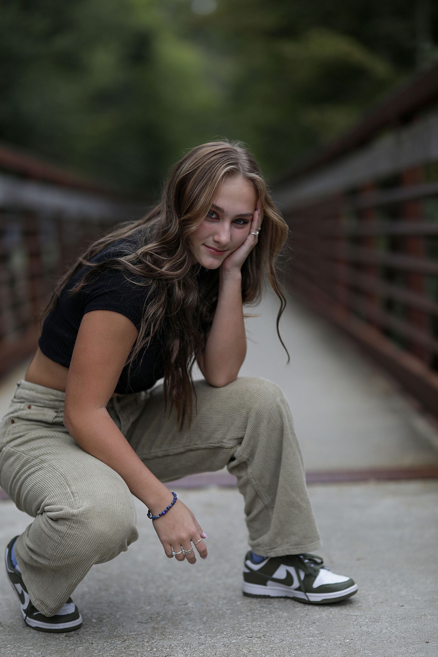 A person in casual attire crouches low on a concrete walkway with trees in the blurred background.