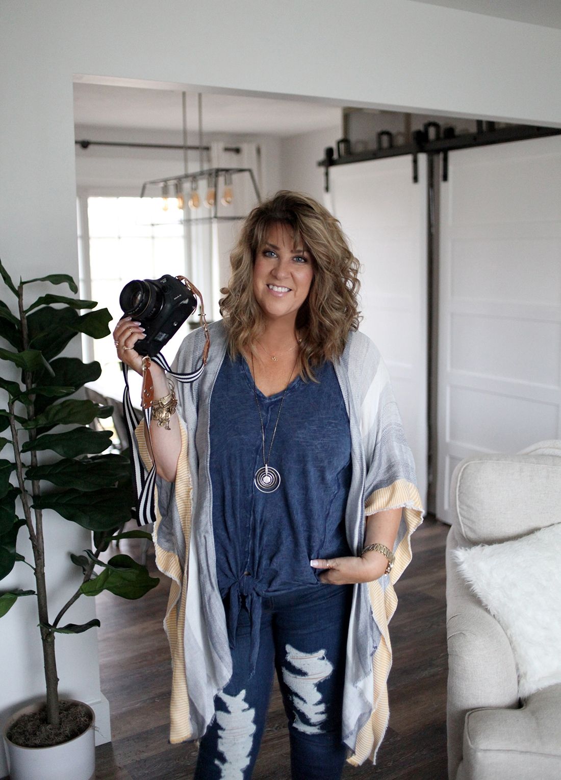 A photographer in casual attire holding a professional camera in a modern home setting.