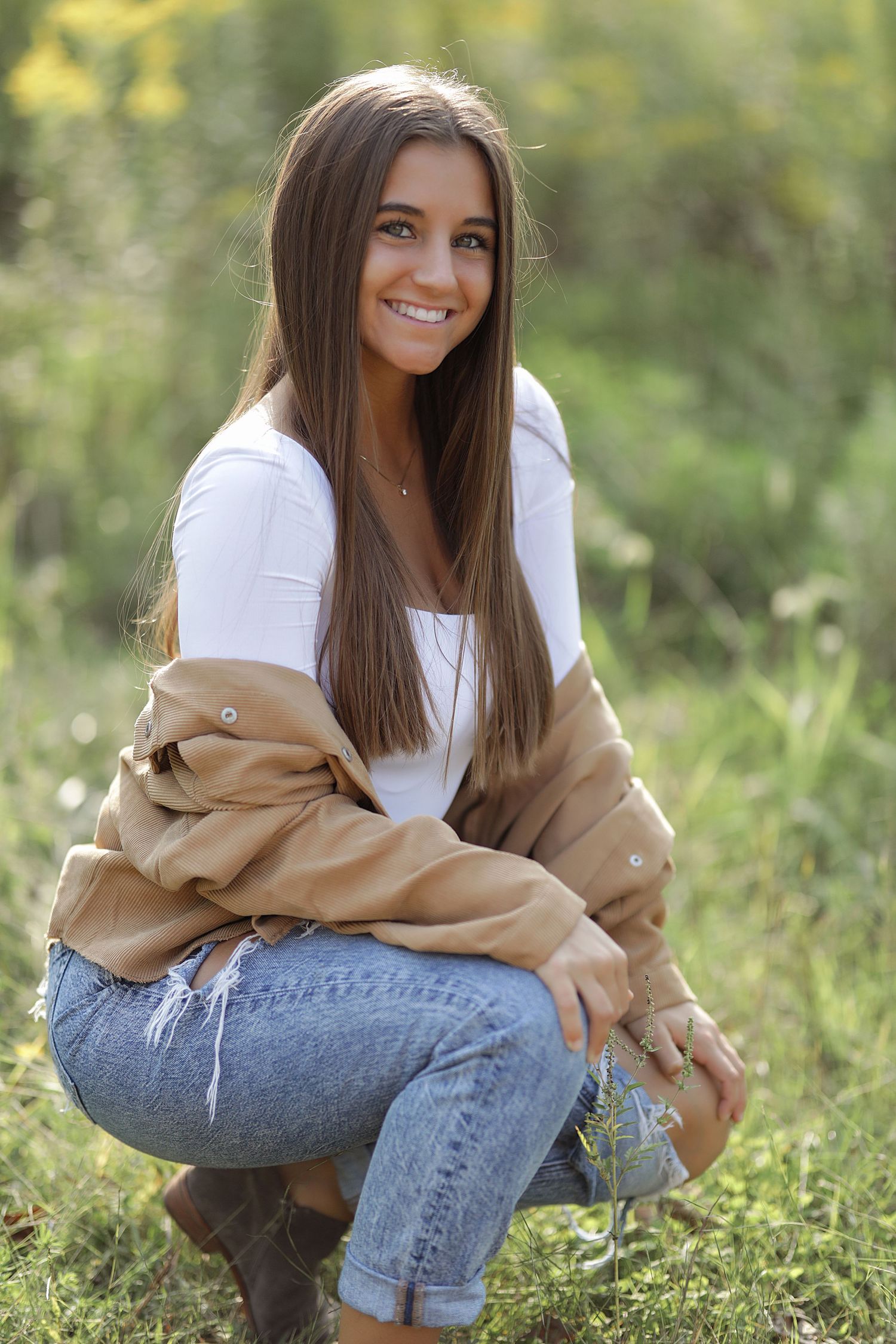 Person in casual white top and beige jacket sitting on grass in natural outdoor setting.