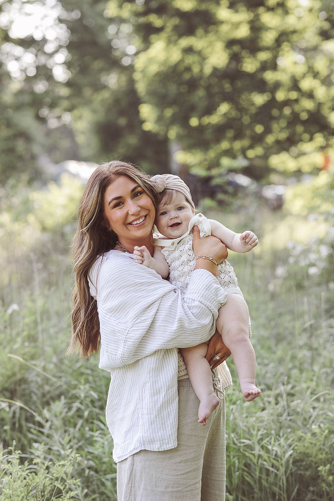 Mother and baby sharing joyful moment together in sunlit meadow wearing coordinated white outfits.