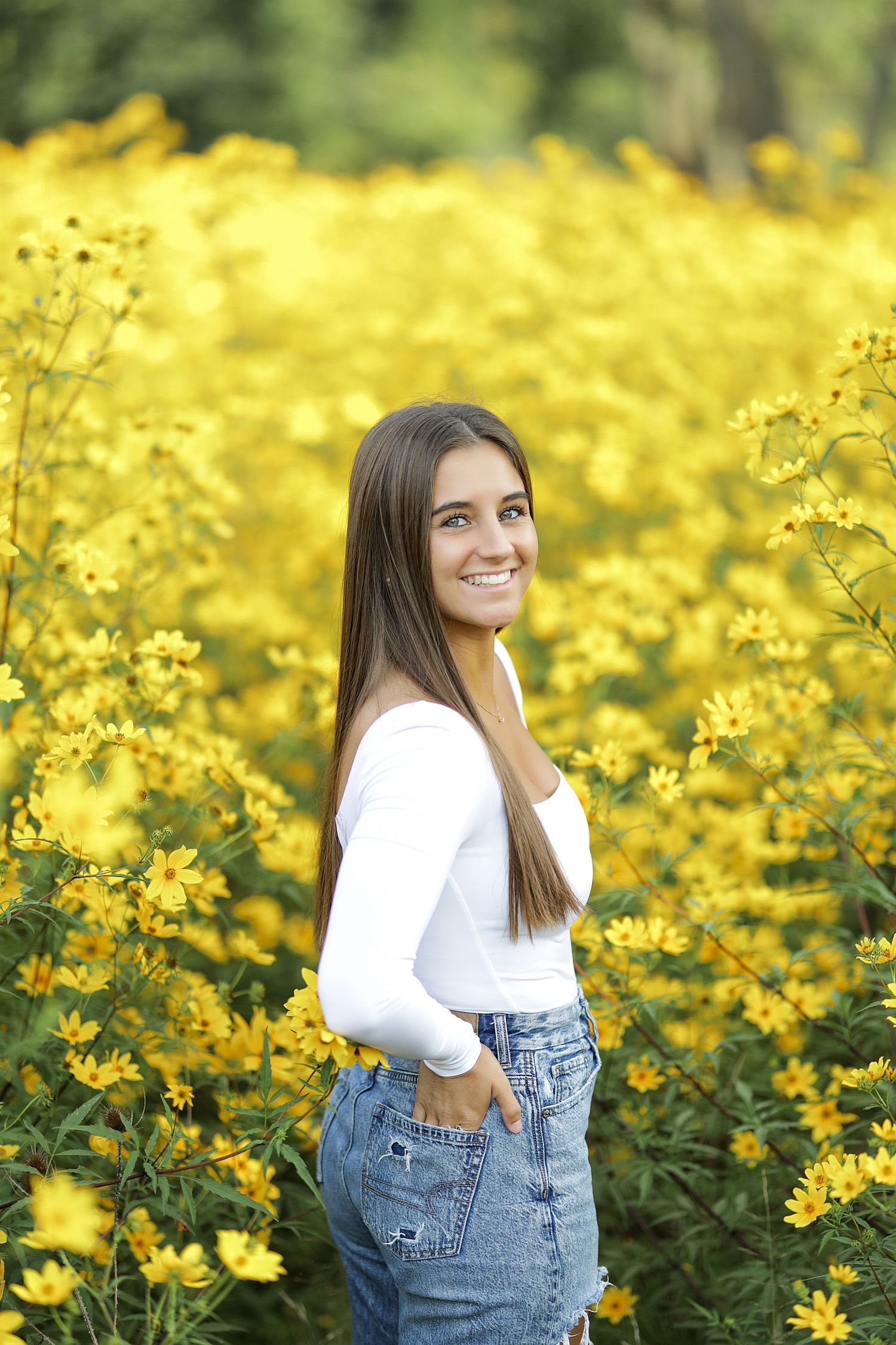 A person in denim overalls stands in a vibrant field of blooming yellow wildflowers on a sunny day.