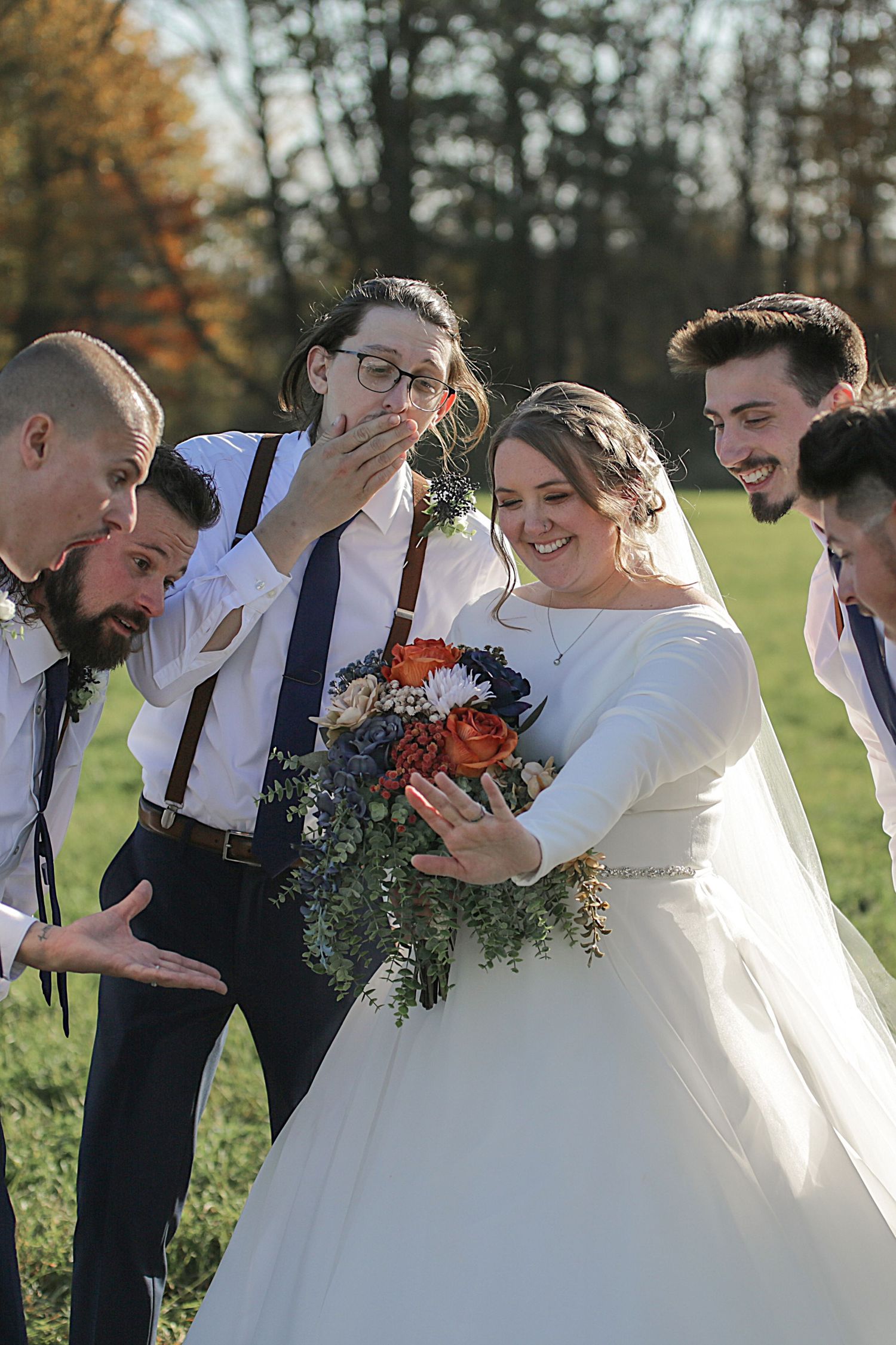 Wedding party in navy and white attire laugh together during candid moment at outdoor celebration.