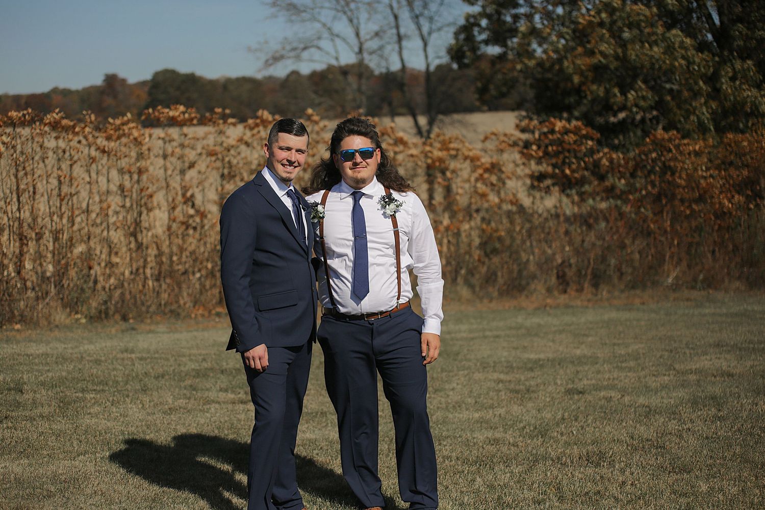 Outdoor wedding photos taken in a field during autumn with trees in the background.