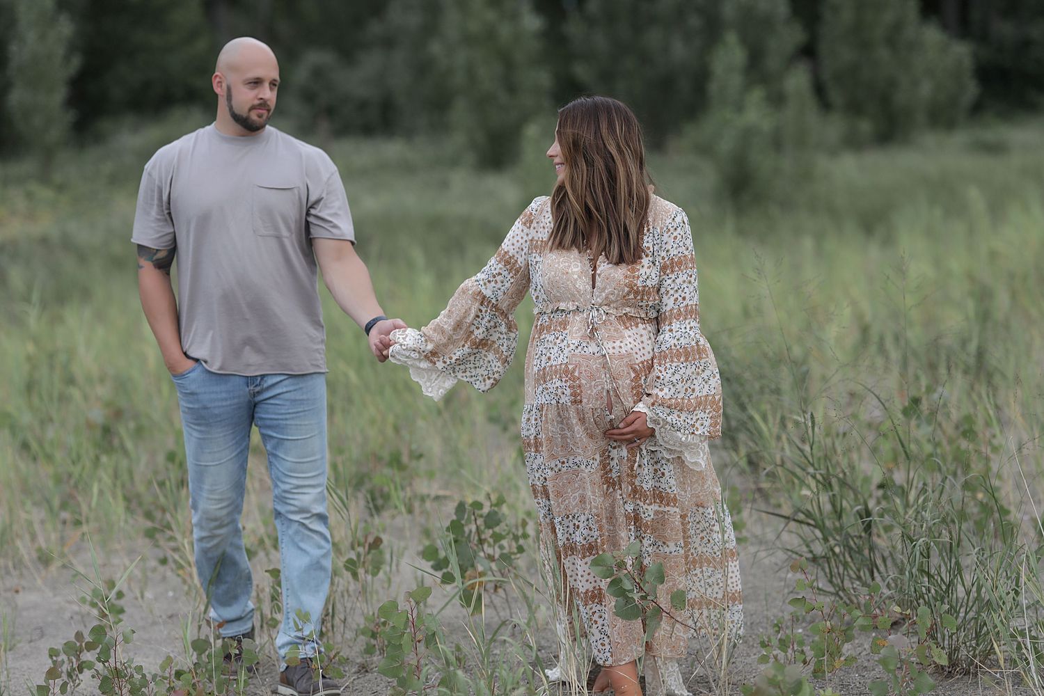 A couple holding hands while walking through a wildflower field on a sunny summer afternoon.