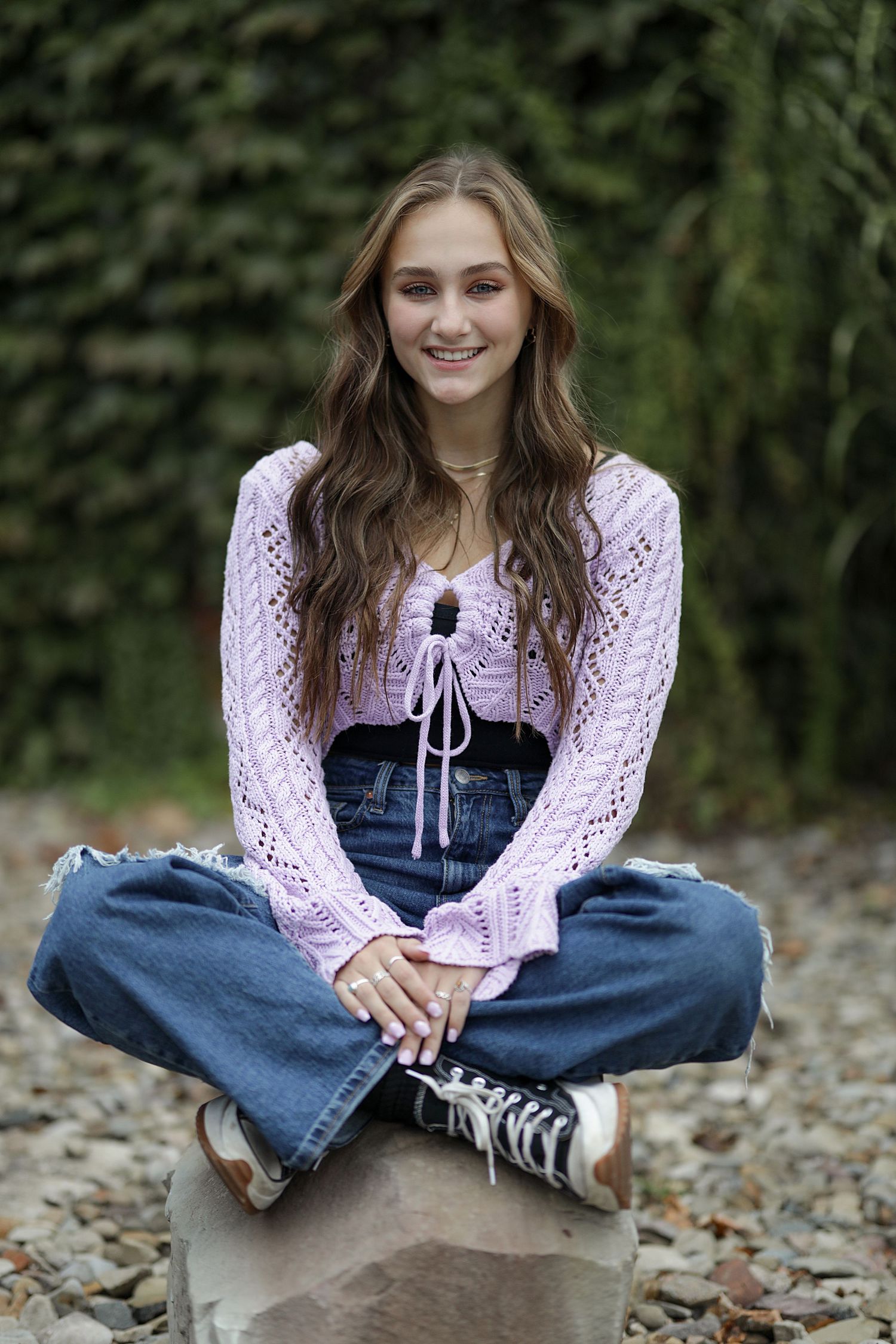 Person in pink knit sweater and jeans sitting on ground with autumn leaves in outdoor setting.