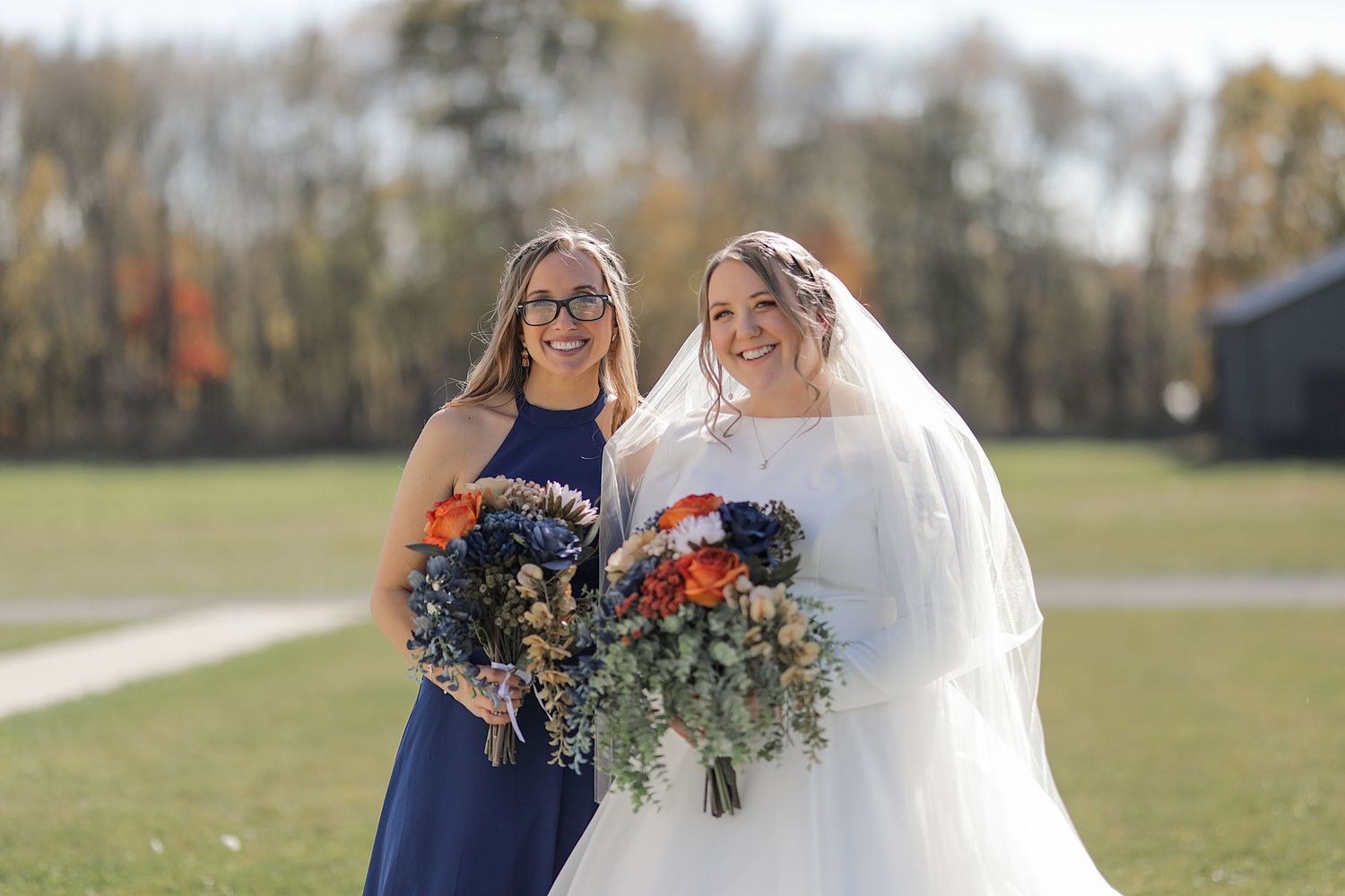 Two people holding beautiful fall-colored bouquets at an outdoor autumn wedding.