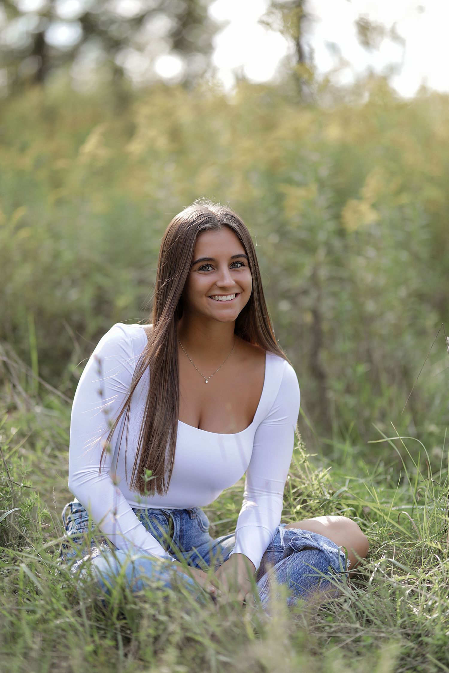Portrait session in a grassy meadow with natural lighting showing someone in a white long-sleeve top and denim.