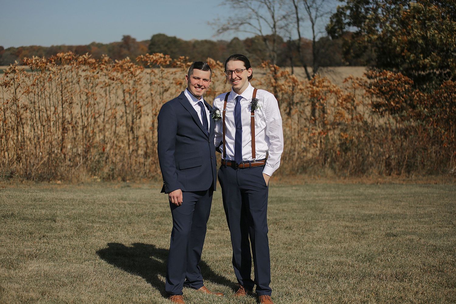Groomsmen in navy suits pose together on grass during fall wedding.