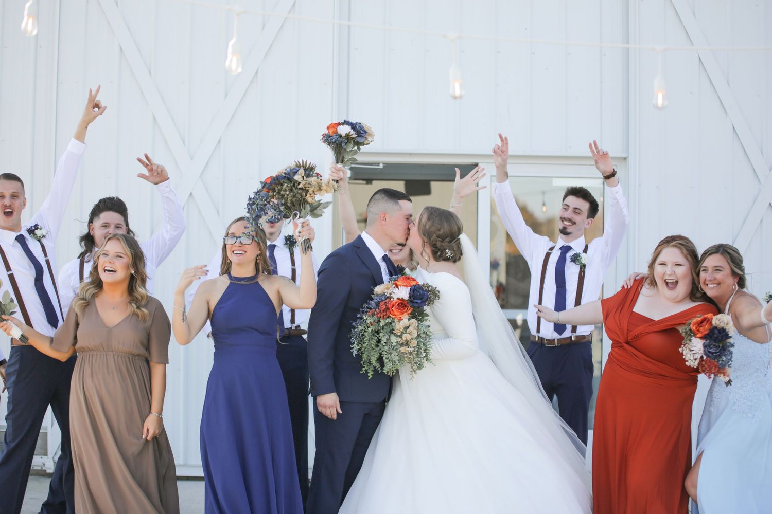 Joyful wedding celebration with party members in coordinated attire against white wall.
