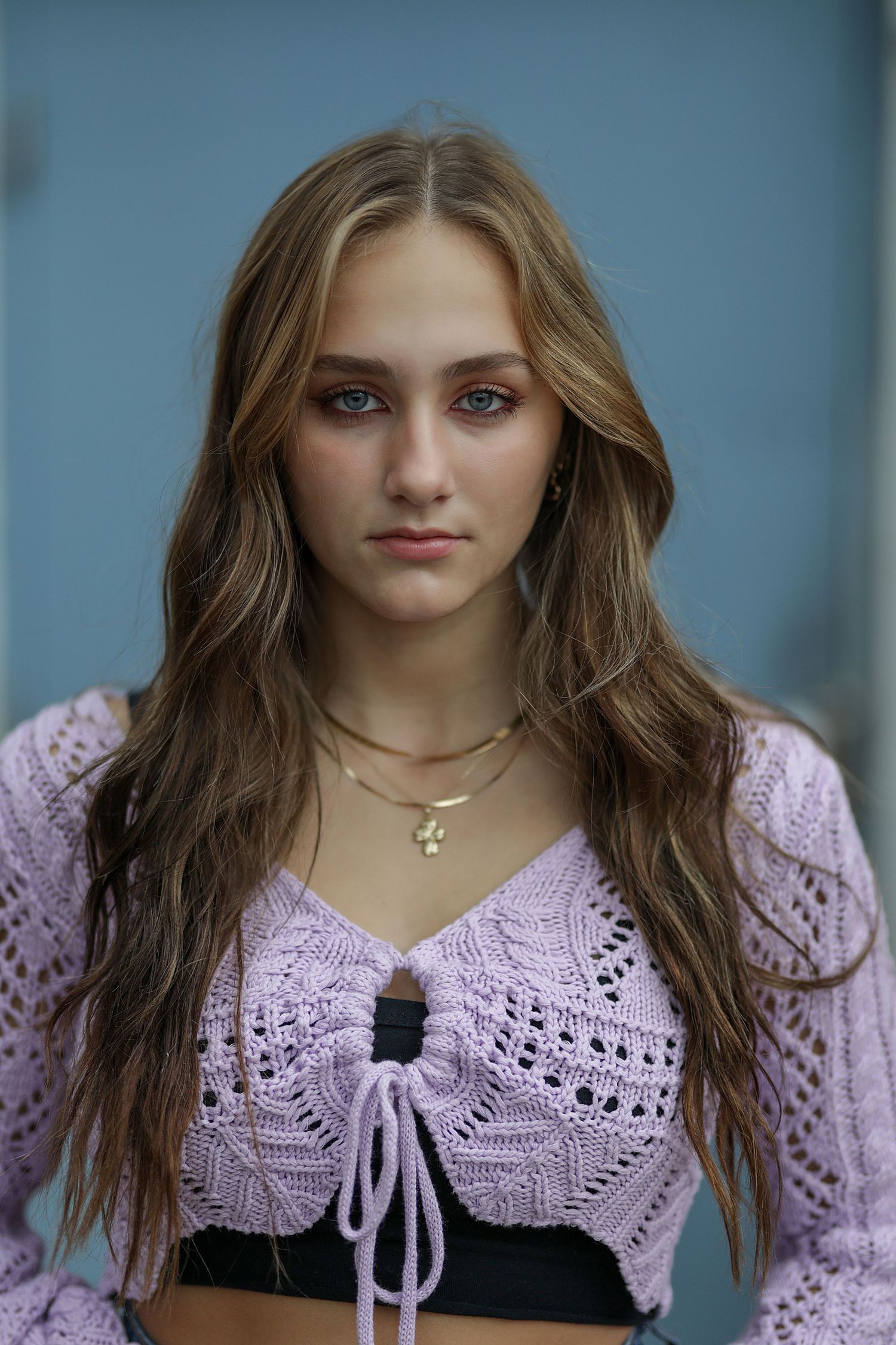 Portrait featuring a pink knit cropped cardigan with bow detail against a blue background.