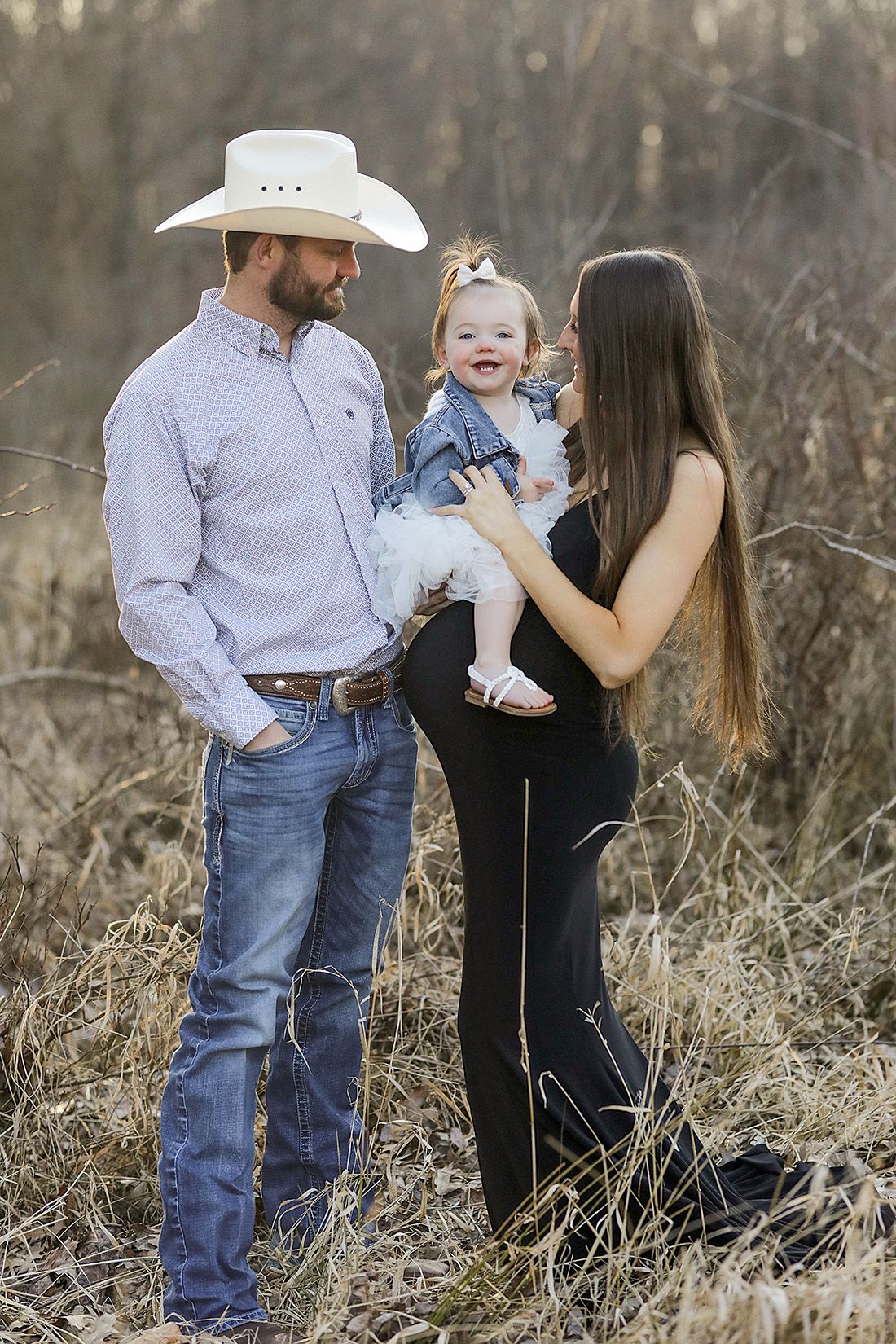 Family photo session in rustic field setting with casual western attire.