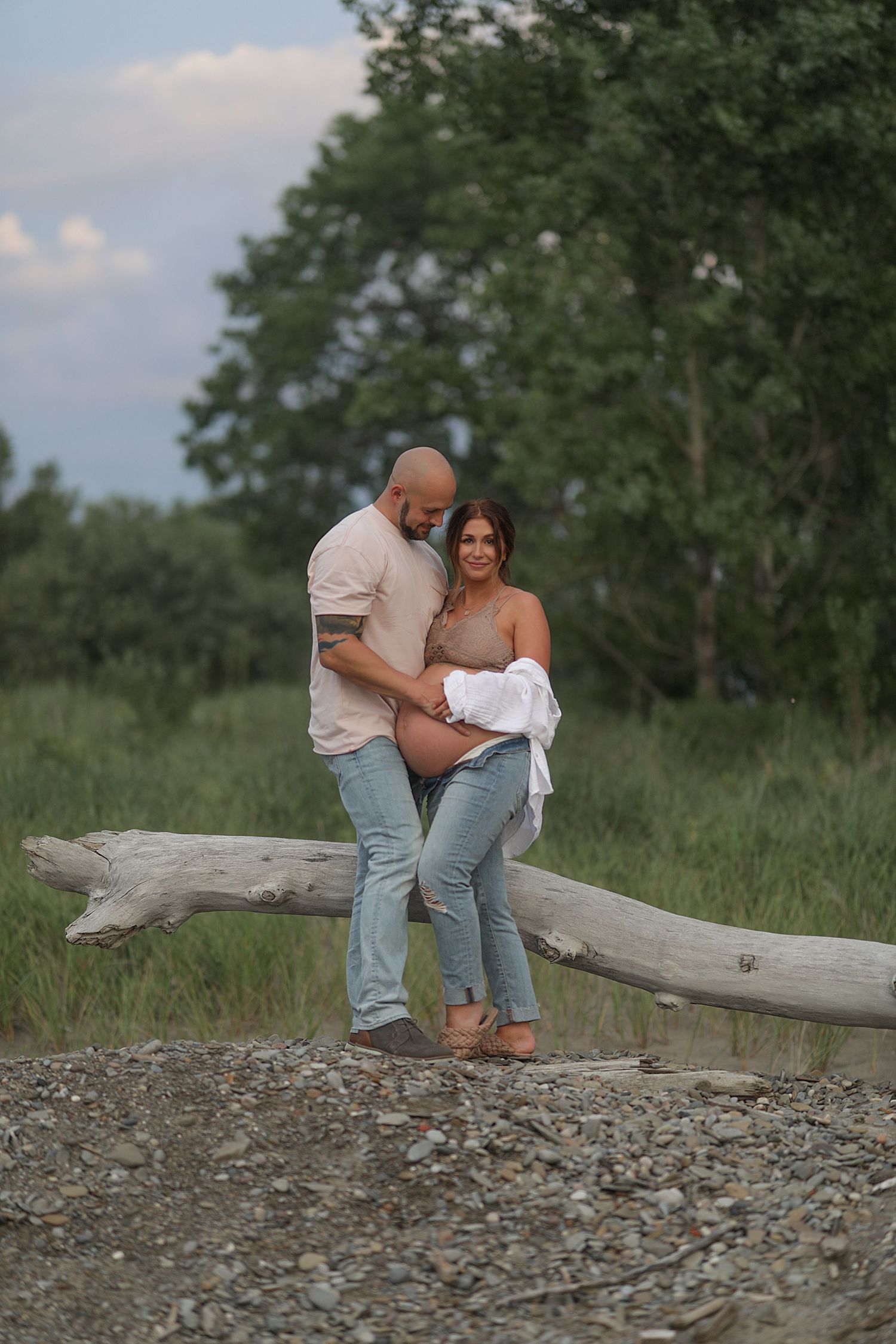 A couple sits together intimately on a fallen log at a rocky beach during golden hour.