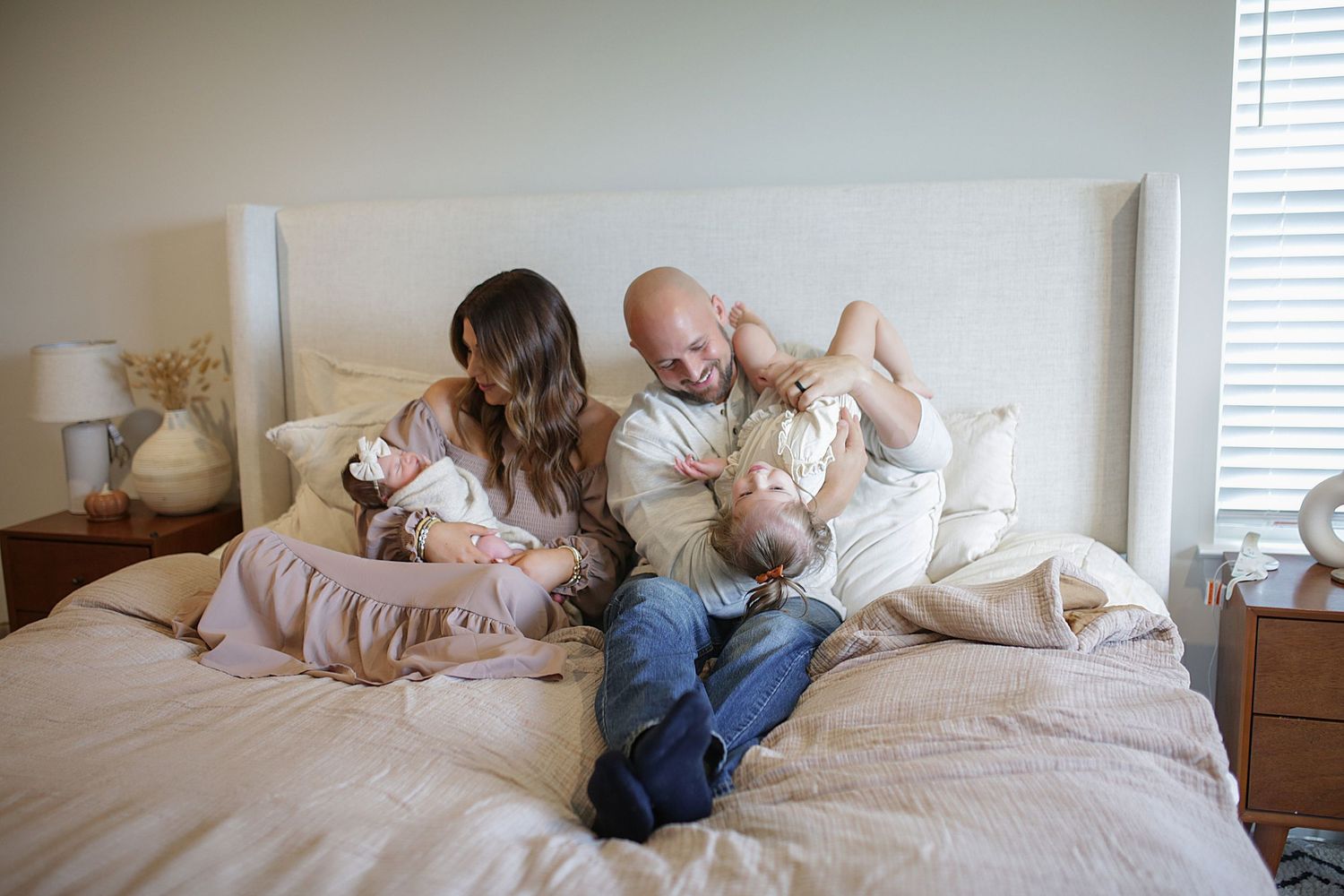 Family enjoying playful moment together while relaxing on bed in bright bedroom.