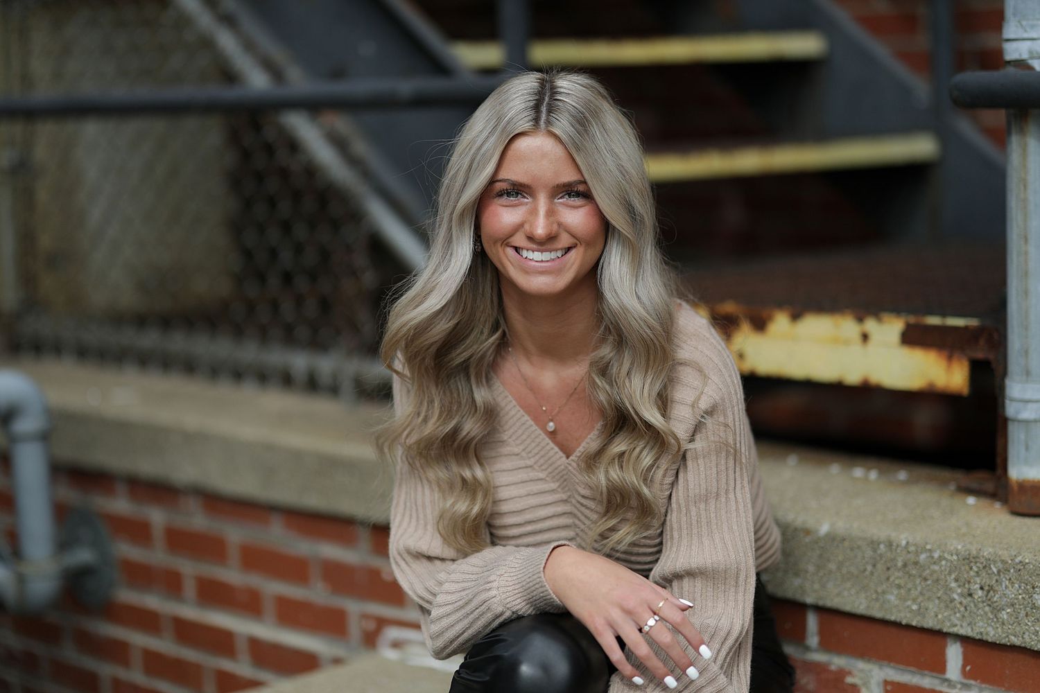 A person in casual attire sits on outdoor brick steps during a photoshoot session.