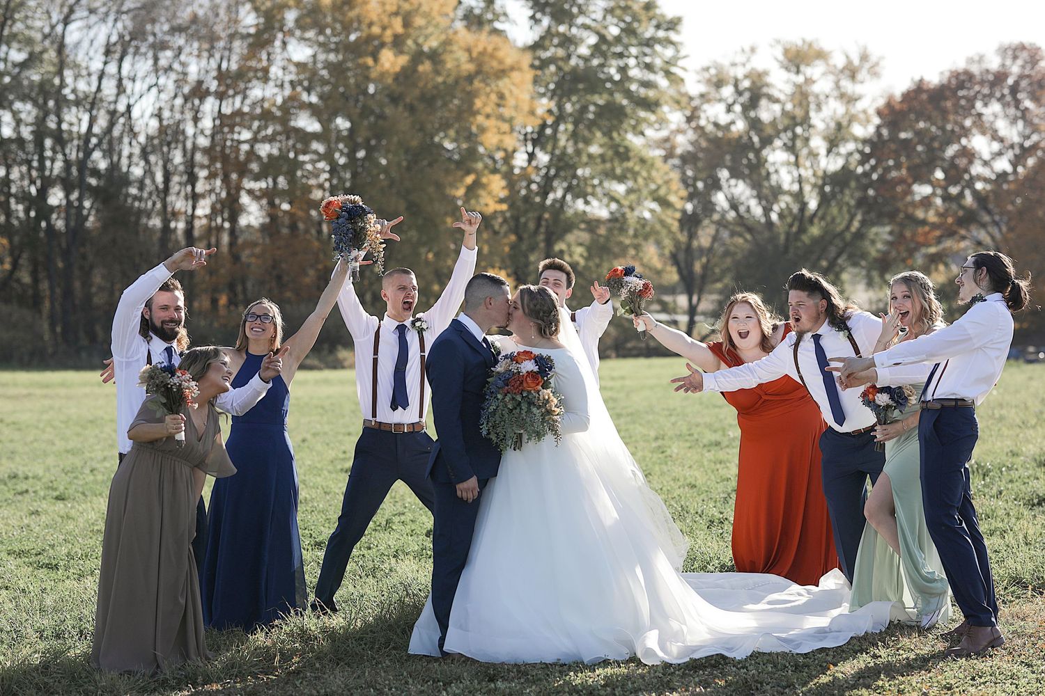 Wedding party celebrating and posing together in a grassy field during autumn.