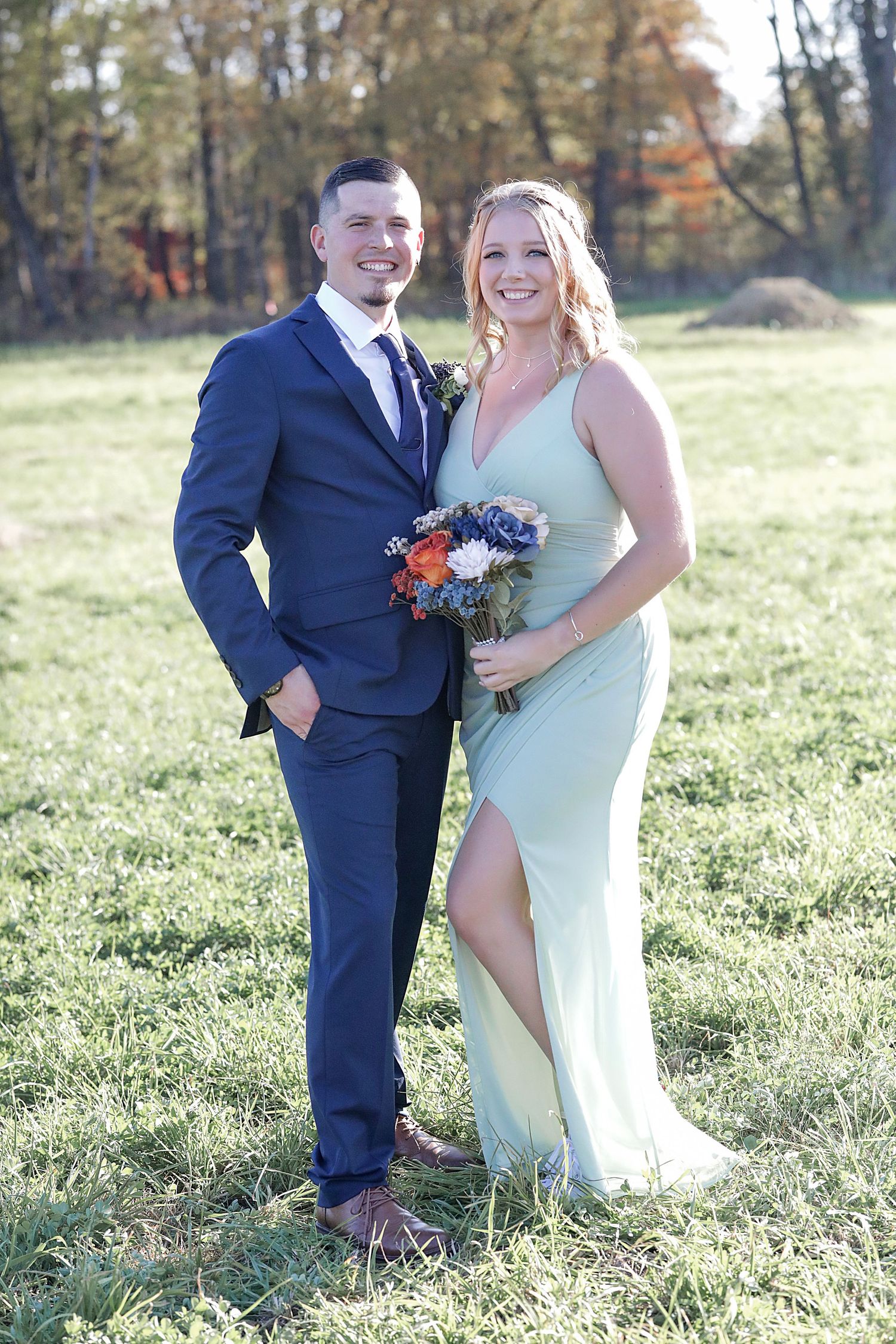 Wedding party members in mint and navy outfits posing in sunny field.